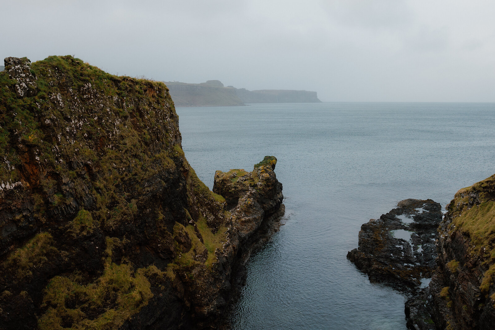 A misty headland rises beyond jagged rock stacks along the shoreline.