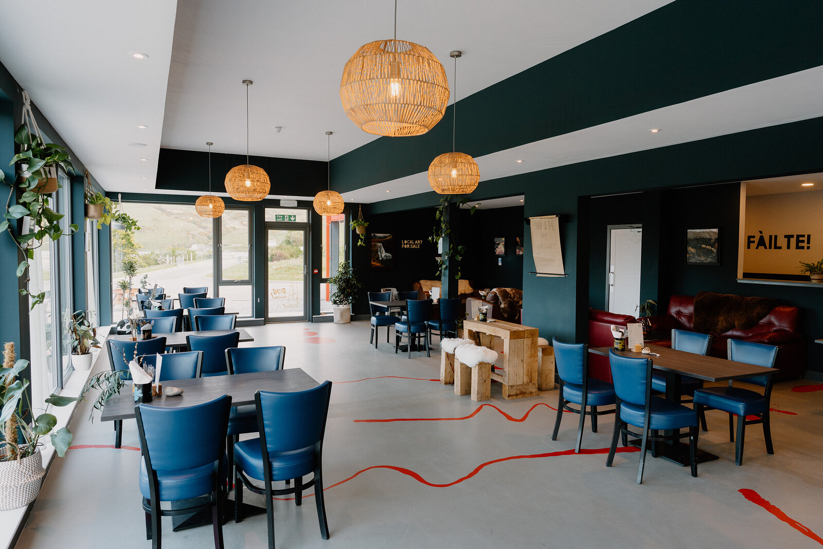 Blue chairs and rattan pendant lamps fill Café Cùil's dining room beside a 'Fàilte!' sign.