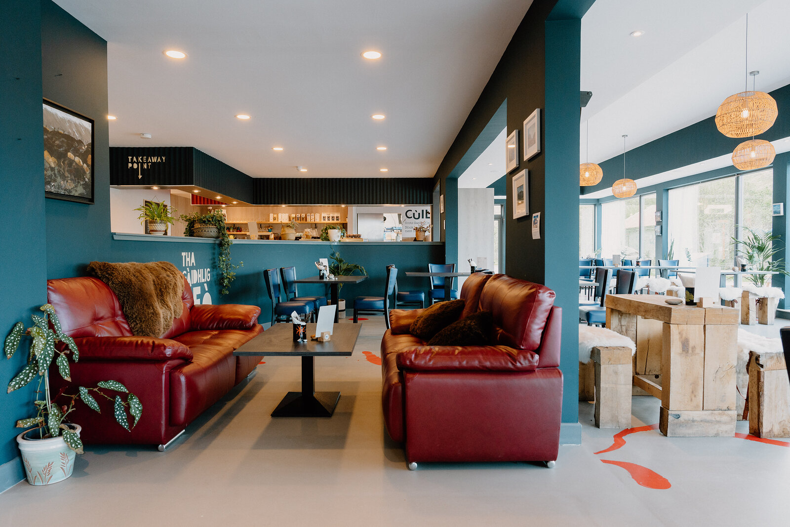 Red leather sofas and a low table furnish a lounge corner of Café Cùil beneath teal walls.