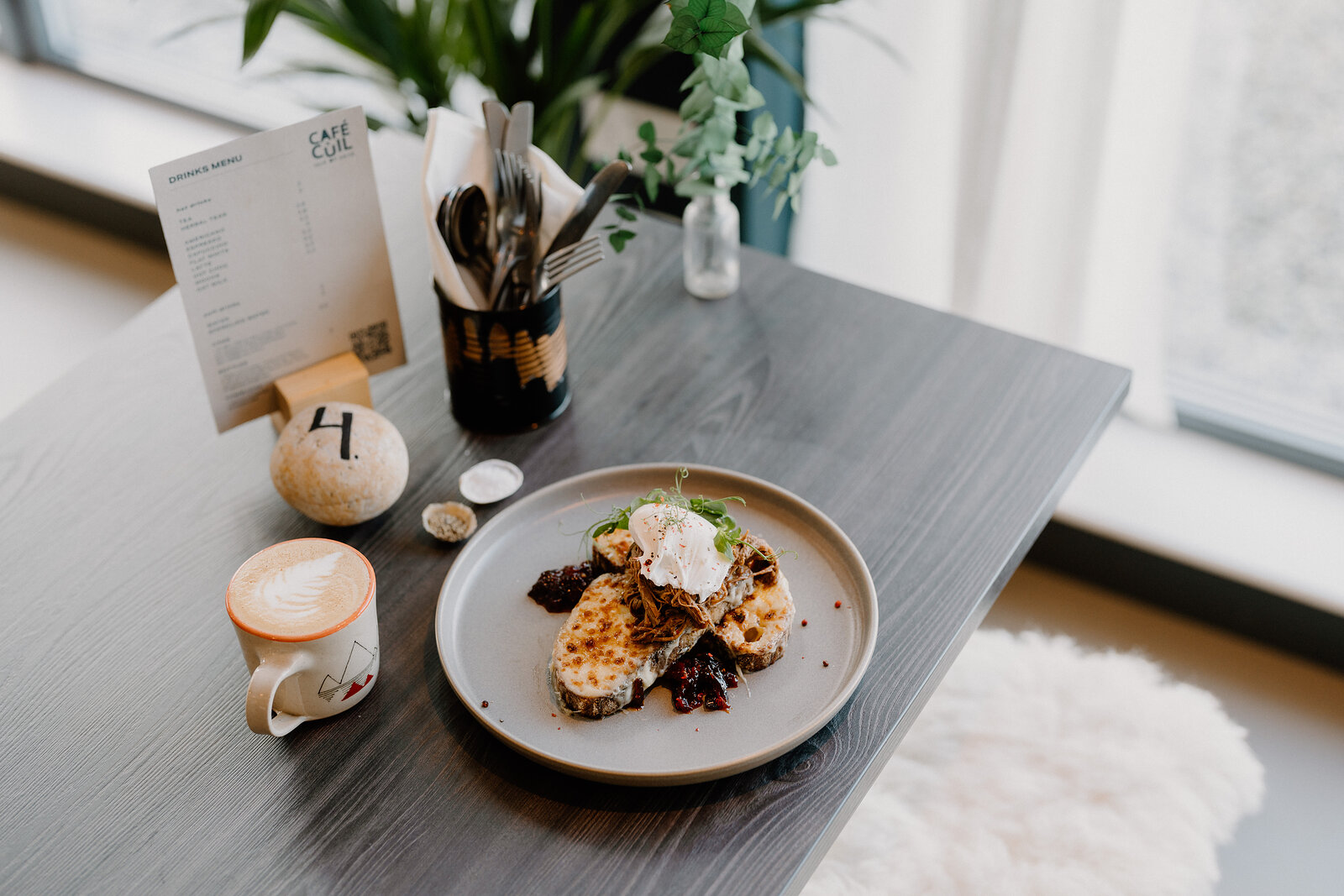 A savoury tart topped with a poached egg sits on a plate beside a latte at Café Cùil.