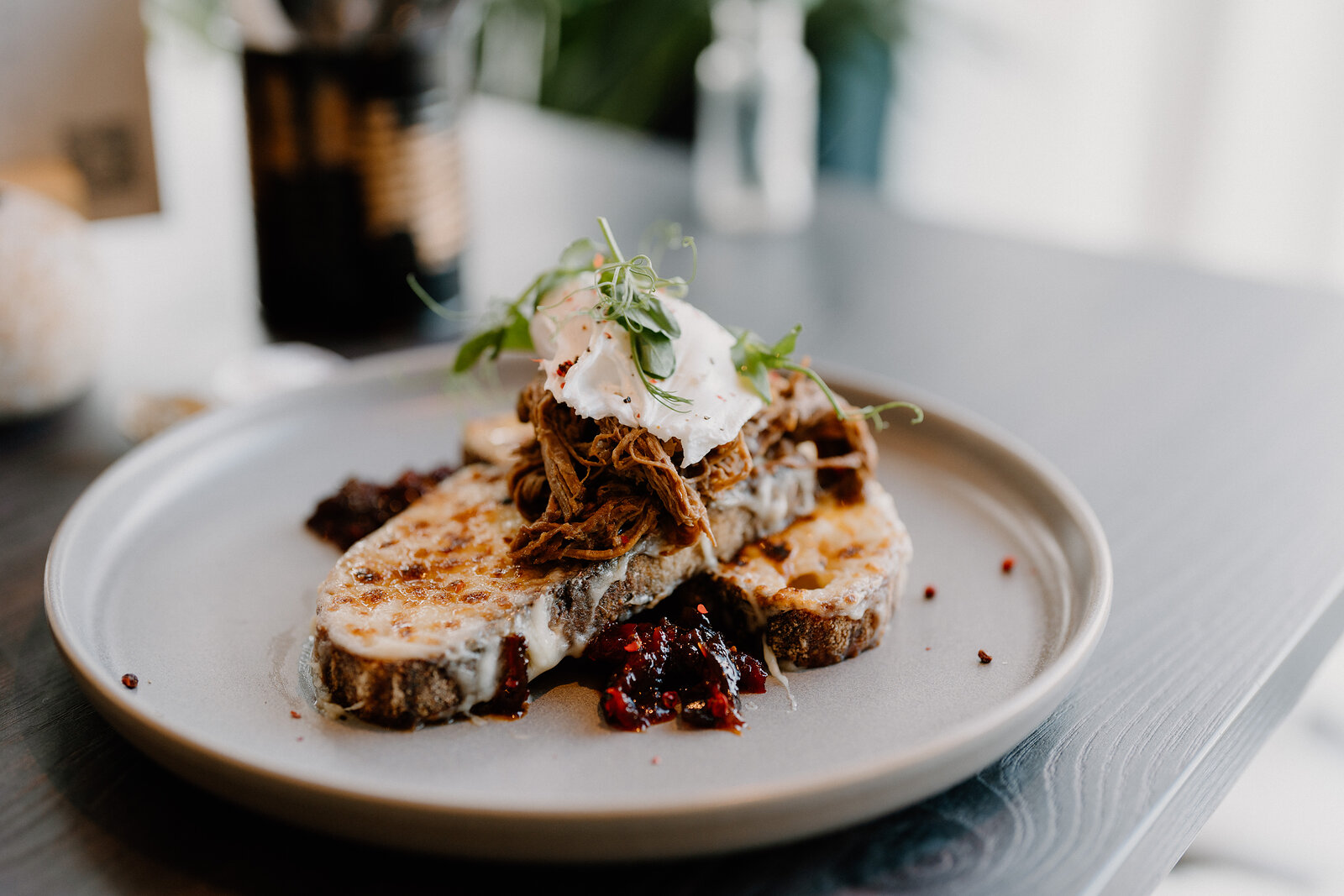 A close-up shows a plated dish of toast topped with pulled meat, poached egg and a berry compote.