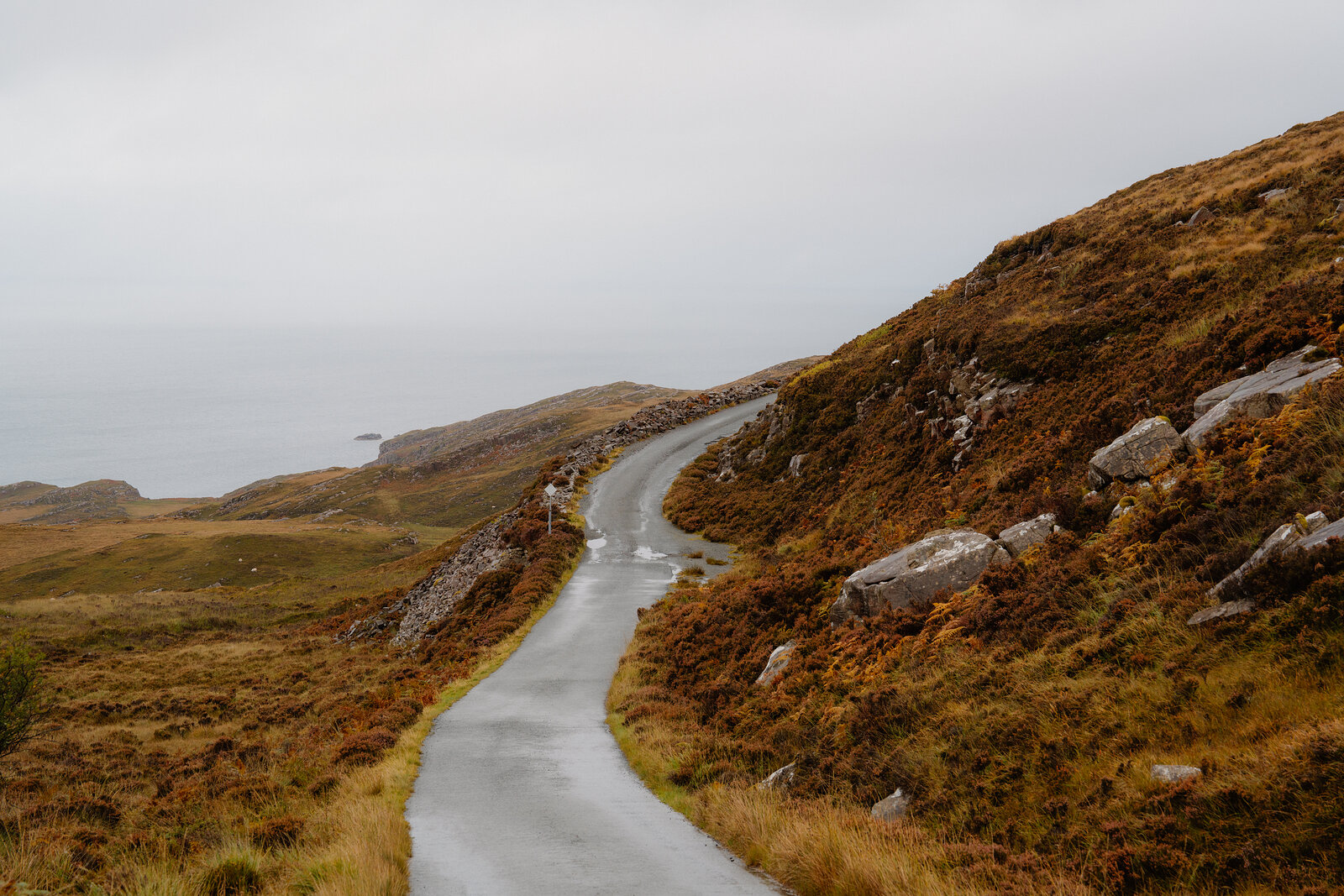 A single-track road winds through rocky moorland toward the coast.