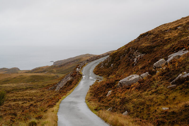 A single-track road winds through rocky moorland toward the coast.