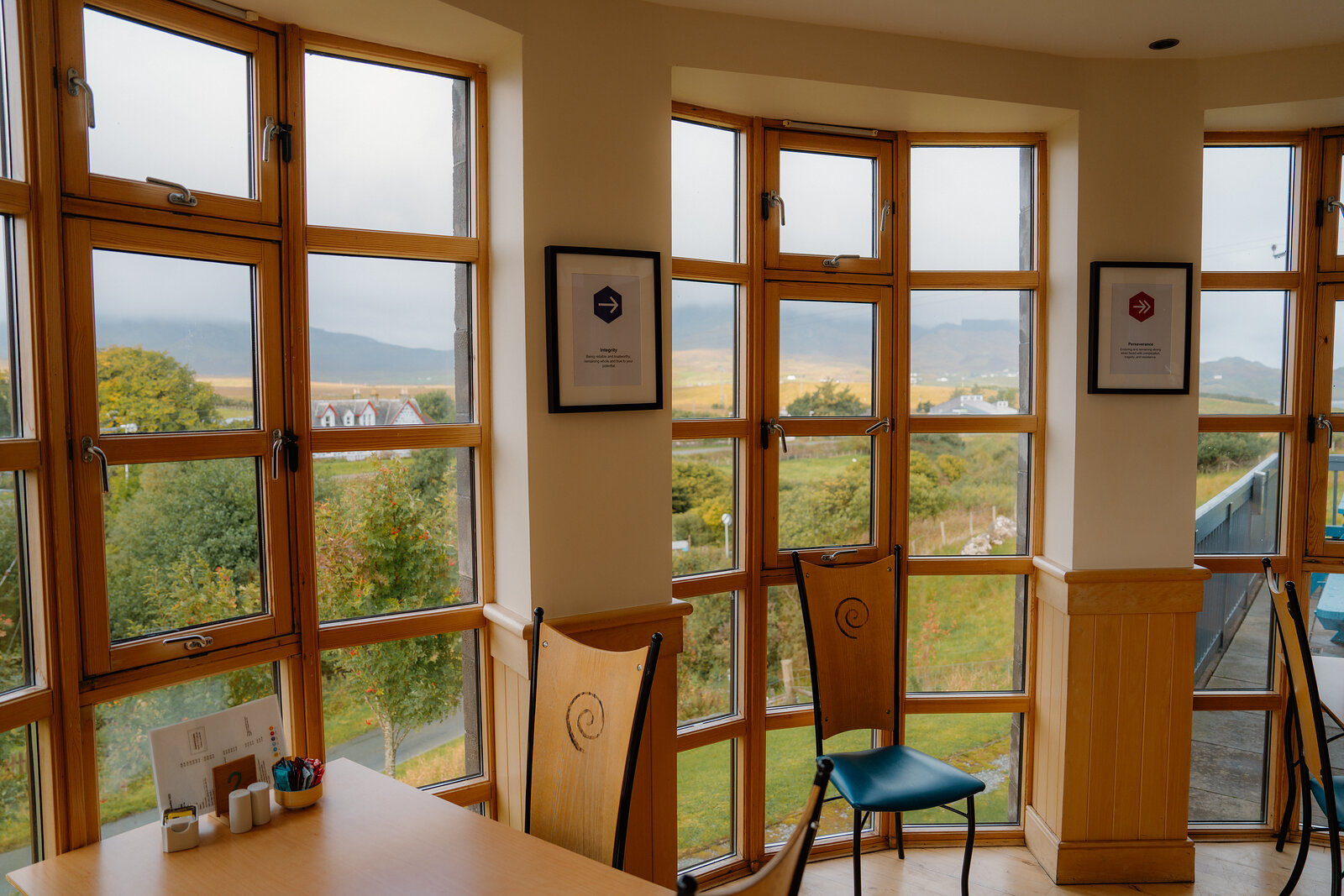 Framed certificates hang beside tall windows overlooking hills in a wood-panelled upper room.