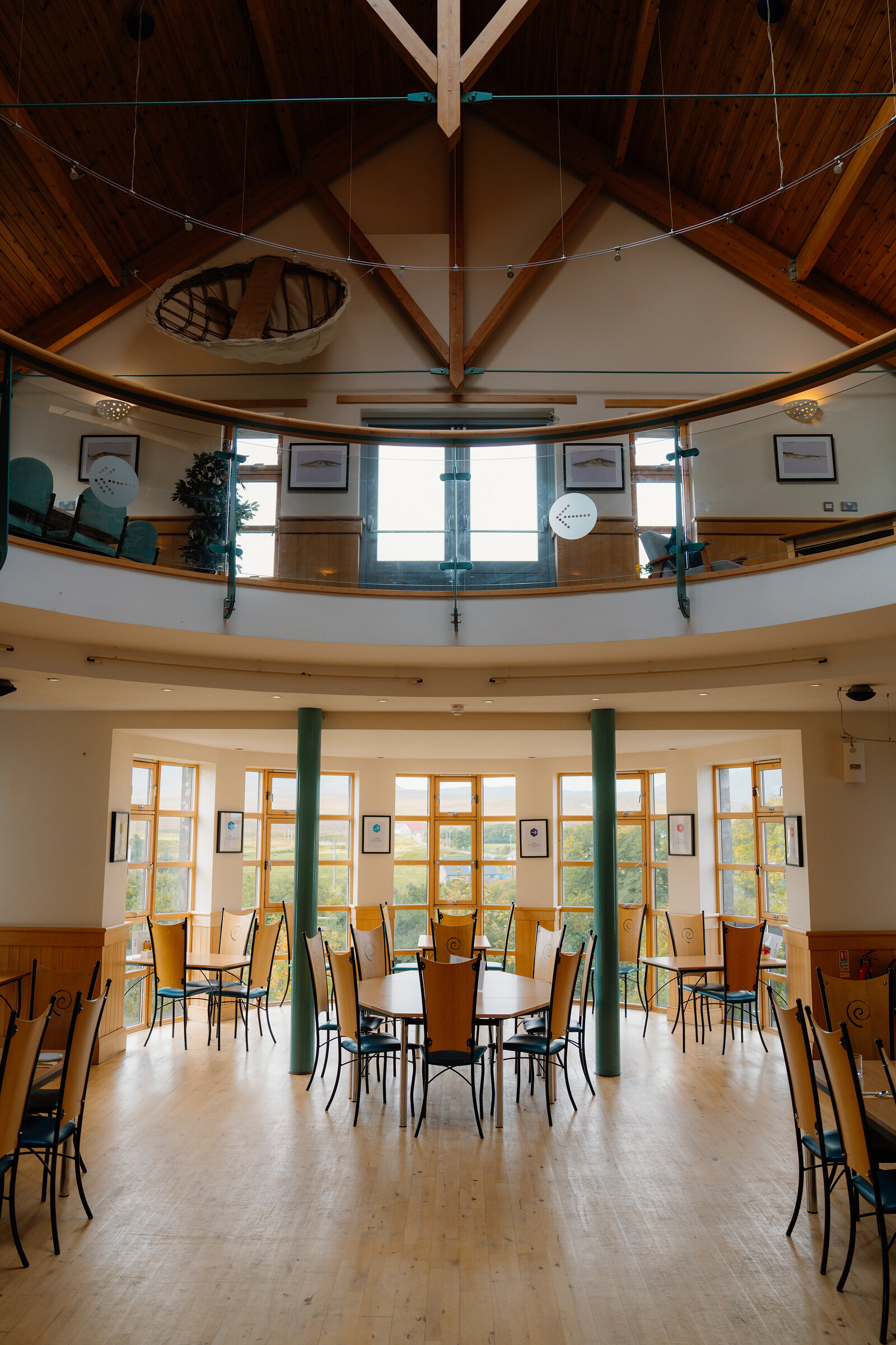A model boat hangs from the timber-raftered ceiling above a circular dining hall with tall windows.