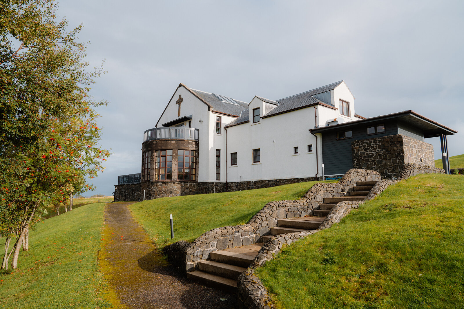 A modern white house with a stone base and steps built into a grassy slope.
