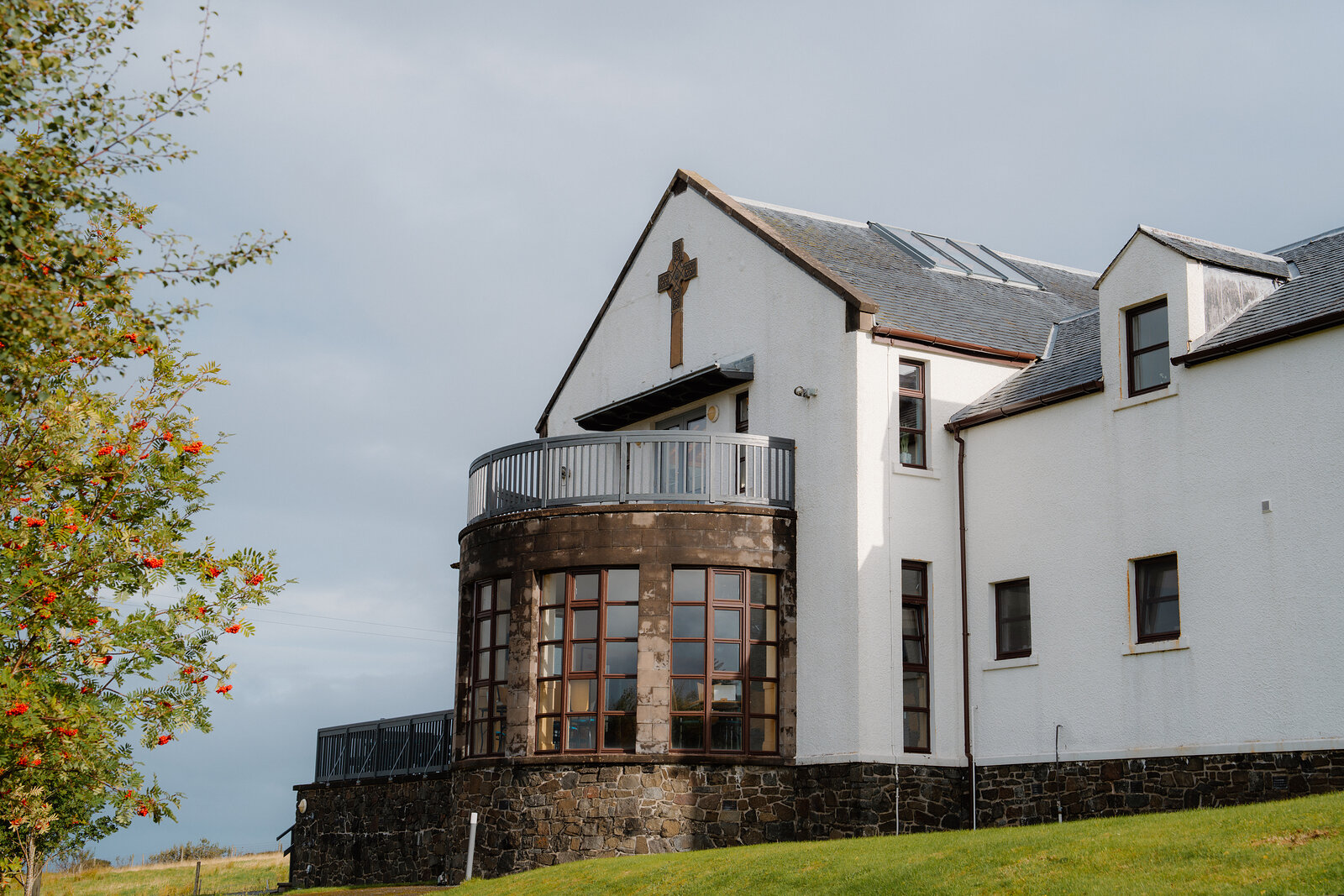 A white building with a cross-shaped gable window and a curved glass conservatory.