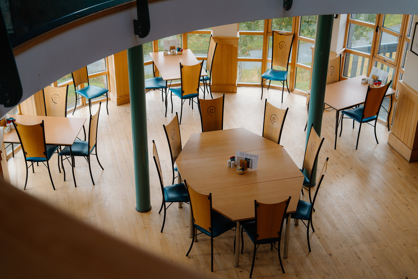 Wooden tables and chairs fill a circular dining hall lit by tall windows.