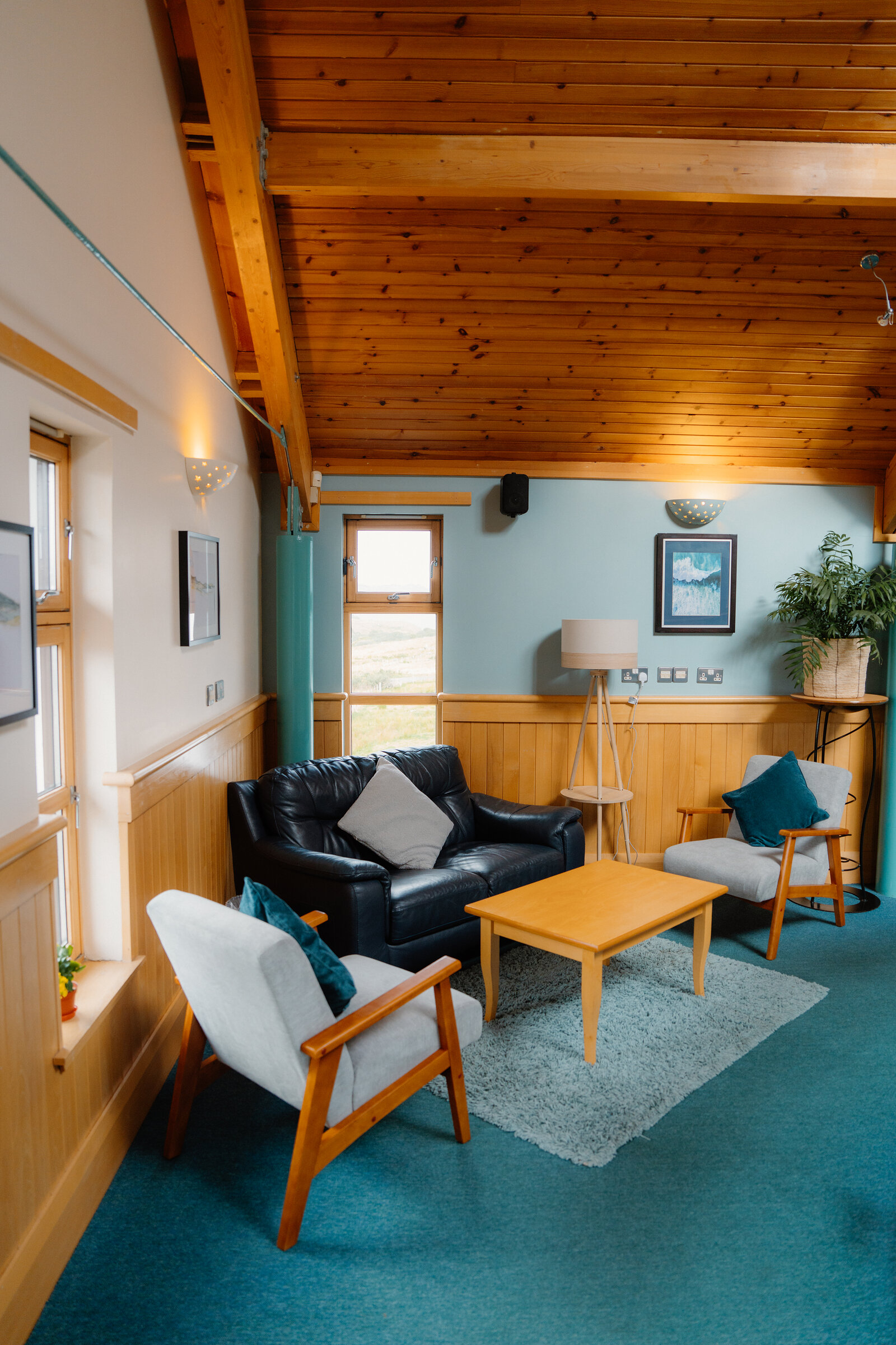 A black leather sofa and armchairs furnish a lounge beneath a wood-beamed ceiling overlooking moorland.