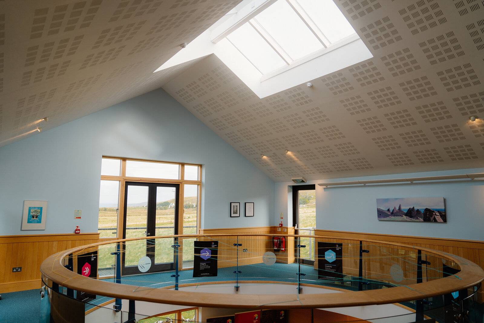 A skylight lights a vaulted white ceiling above a mezzanine hung with framed prints.
