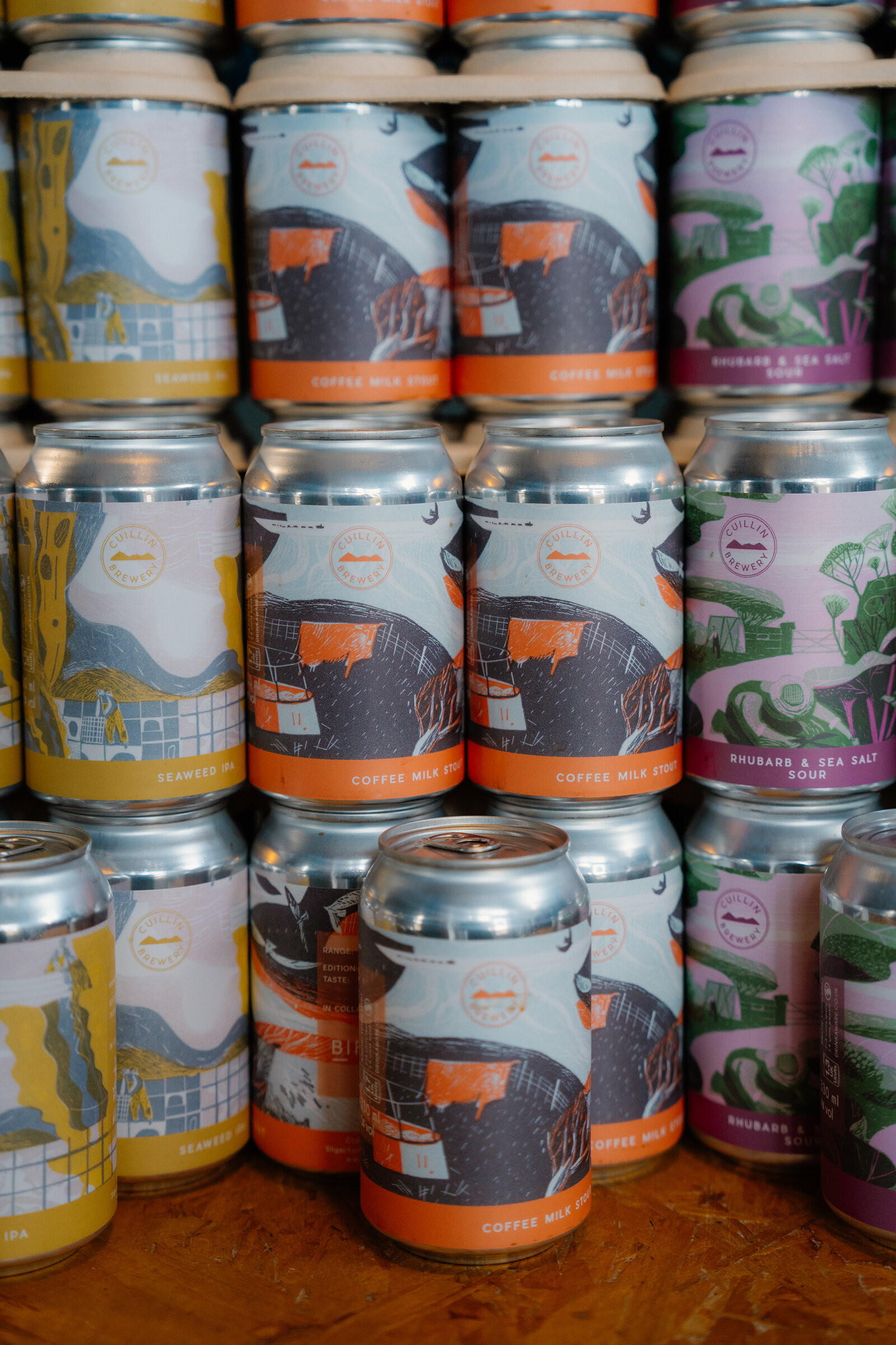 Stacked cans of Cuillin Brewery beer show flavours including coffee milk stout, rhubarb and sea salt sour, and a seaweed IPA.