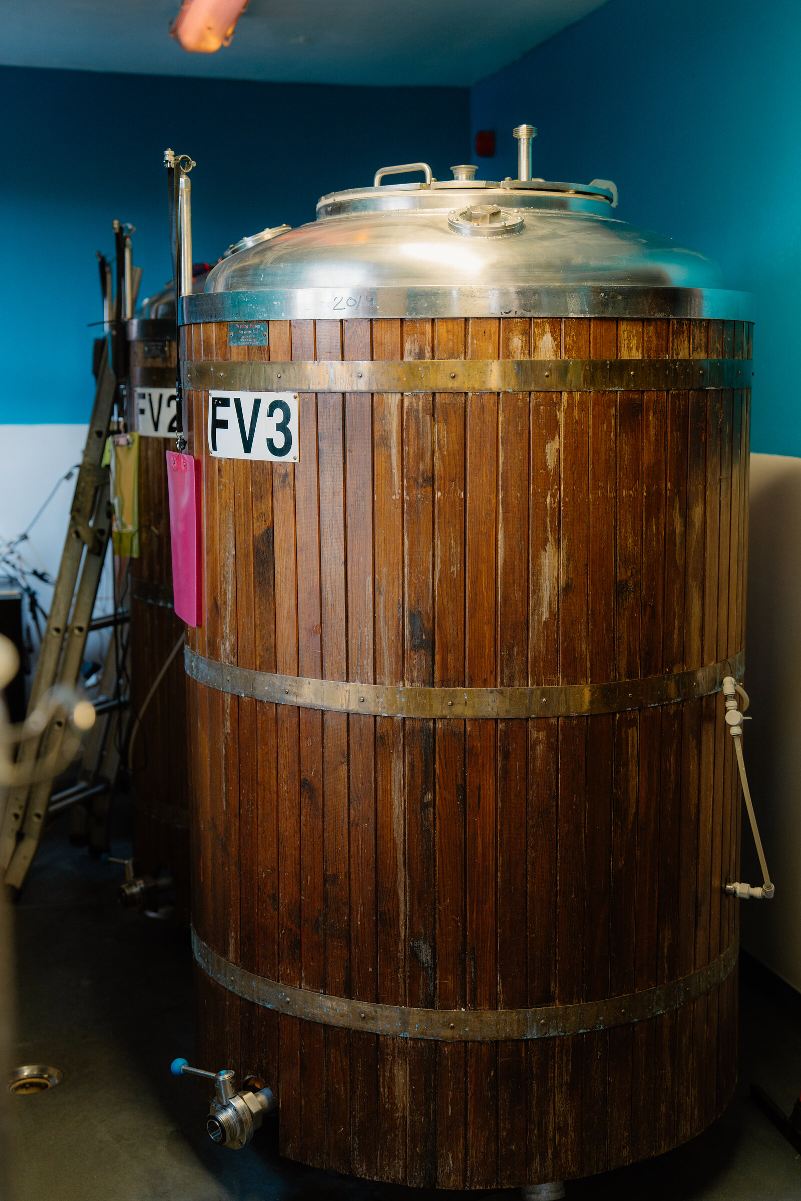 A wooden fermentation vessel labelled FV3 with a stainless steel lid stands in a row of tanks at Cuillin Brewery.