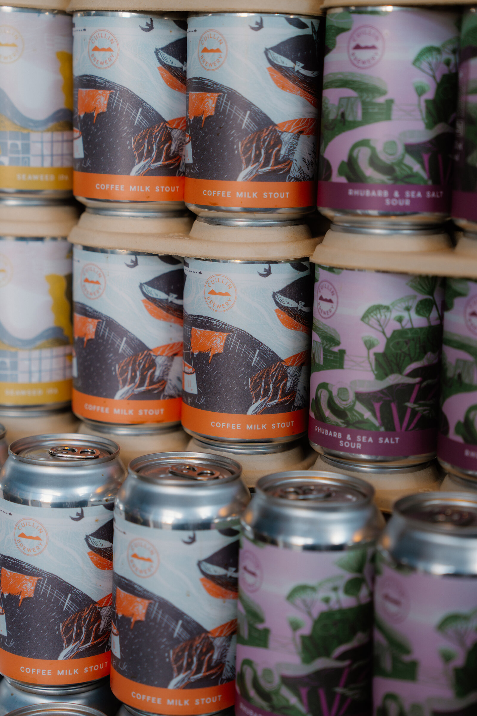 Cans of Cuillin Brewery coffee milk stout and rhubarb and sea salt sour are stacked closely together.