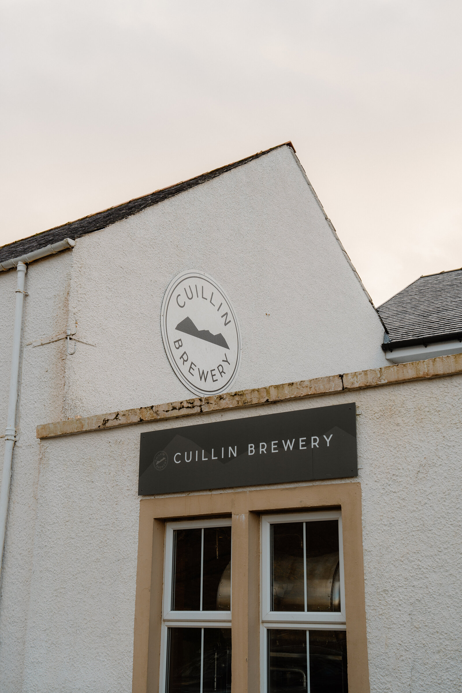 A circular logo with a mountain silhouette and the words 'Cuillin Brewery' is painted above a matching sign on a whitewashed gable.