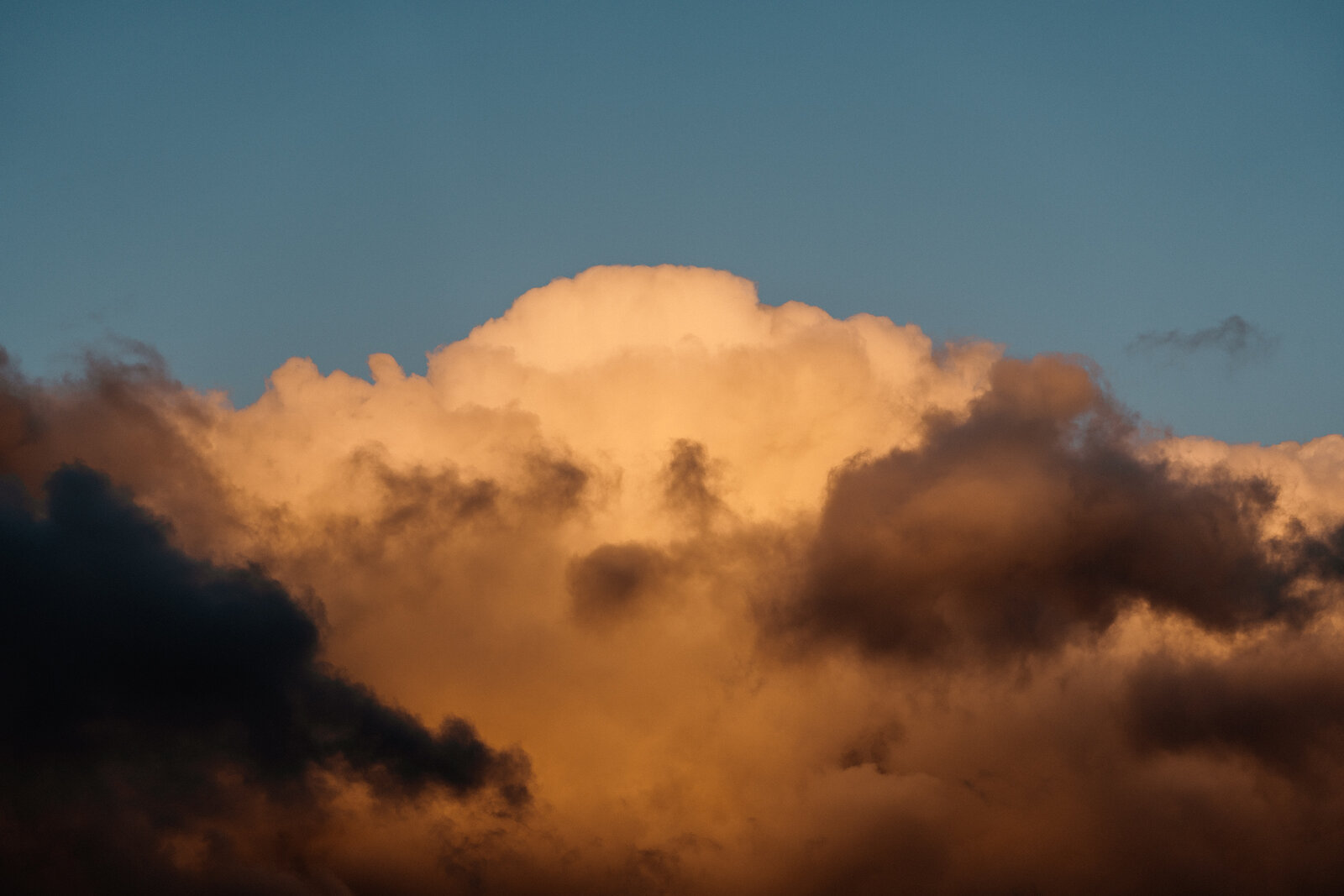 Backlit clouds glow gold and grey against a clear blue sky at sunset.