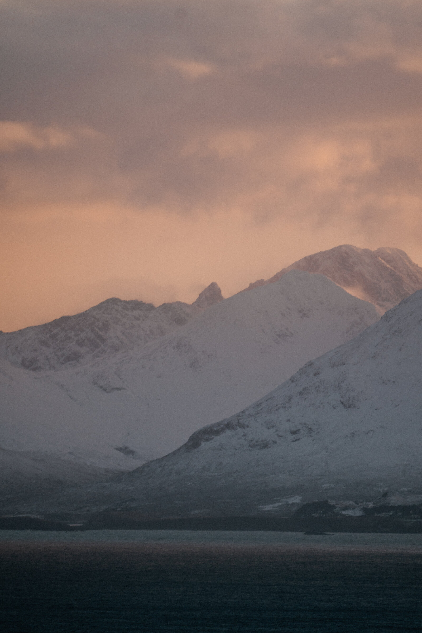 Snow-covered mountain peaks glow pink beneath a band of cloud at dusk.