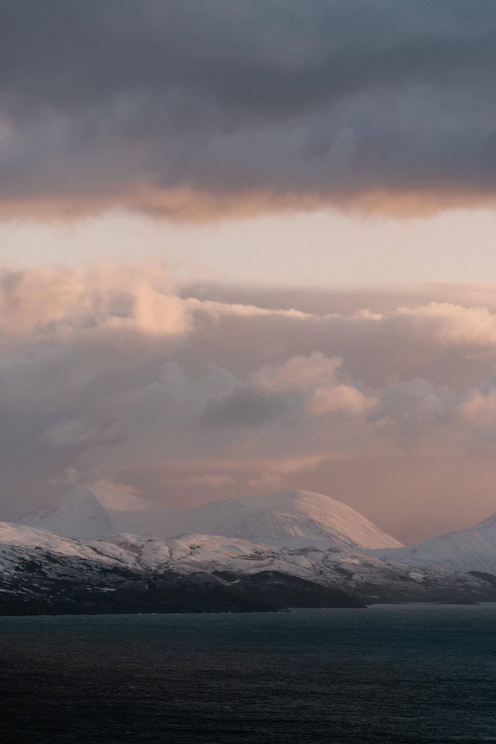Storm clouds hang low over snow-dusted hills bordering a sea loch.