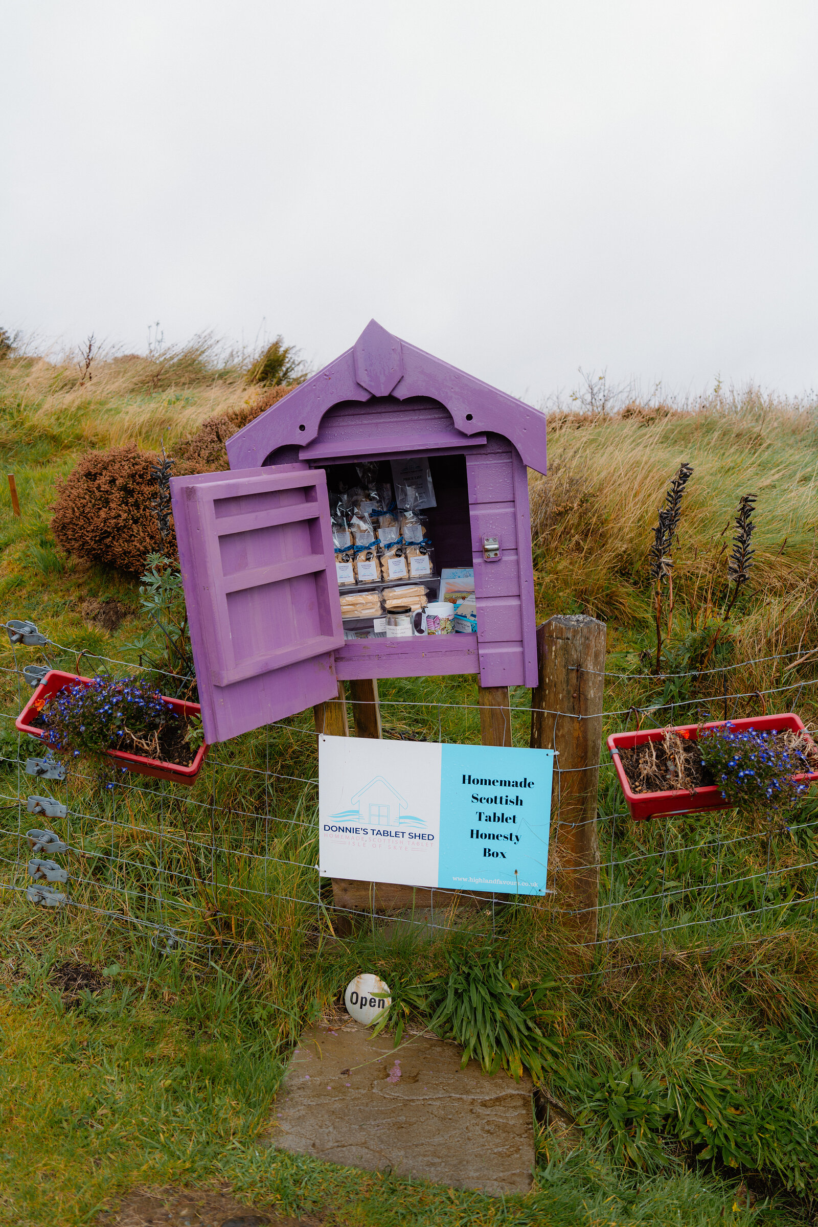 A purple honesty-box shed labelled 'Donnie's Tablet Shed' offers homemade Scottish tablet beside a wire fence.