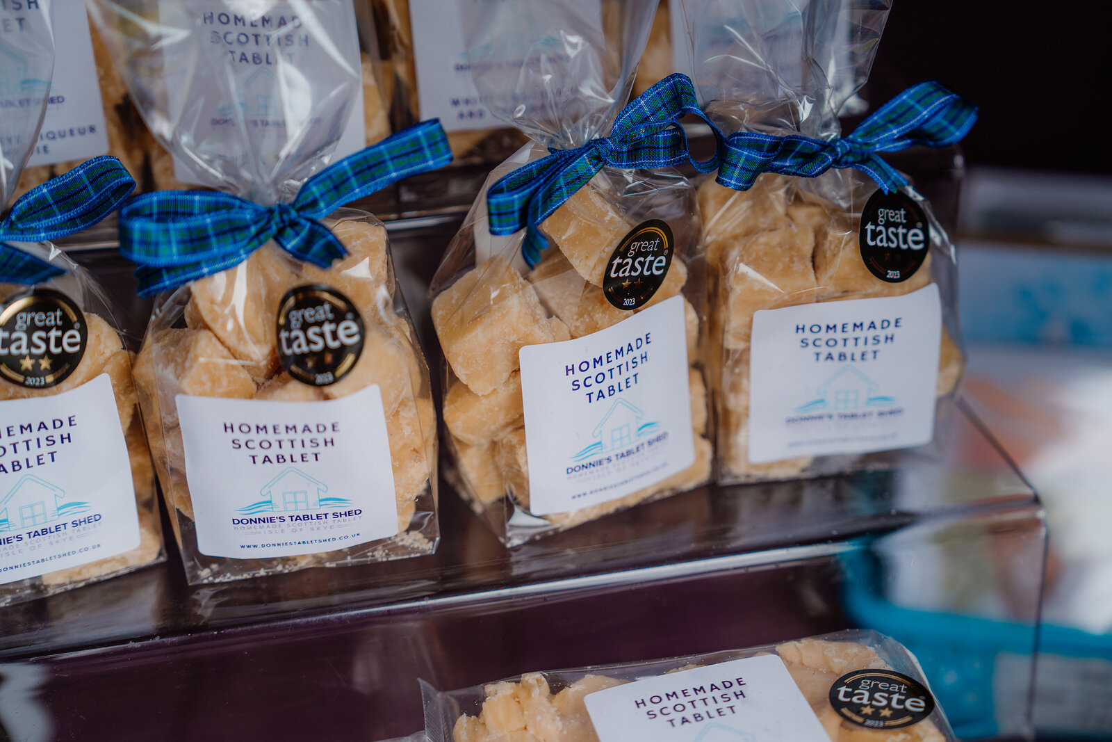 Bags of homemade Scottish tablet tied with tartan bows are labelled 'Donnie's Tablet Shed' on a shelf.