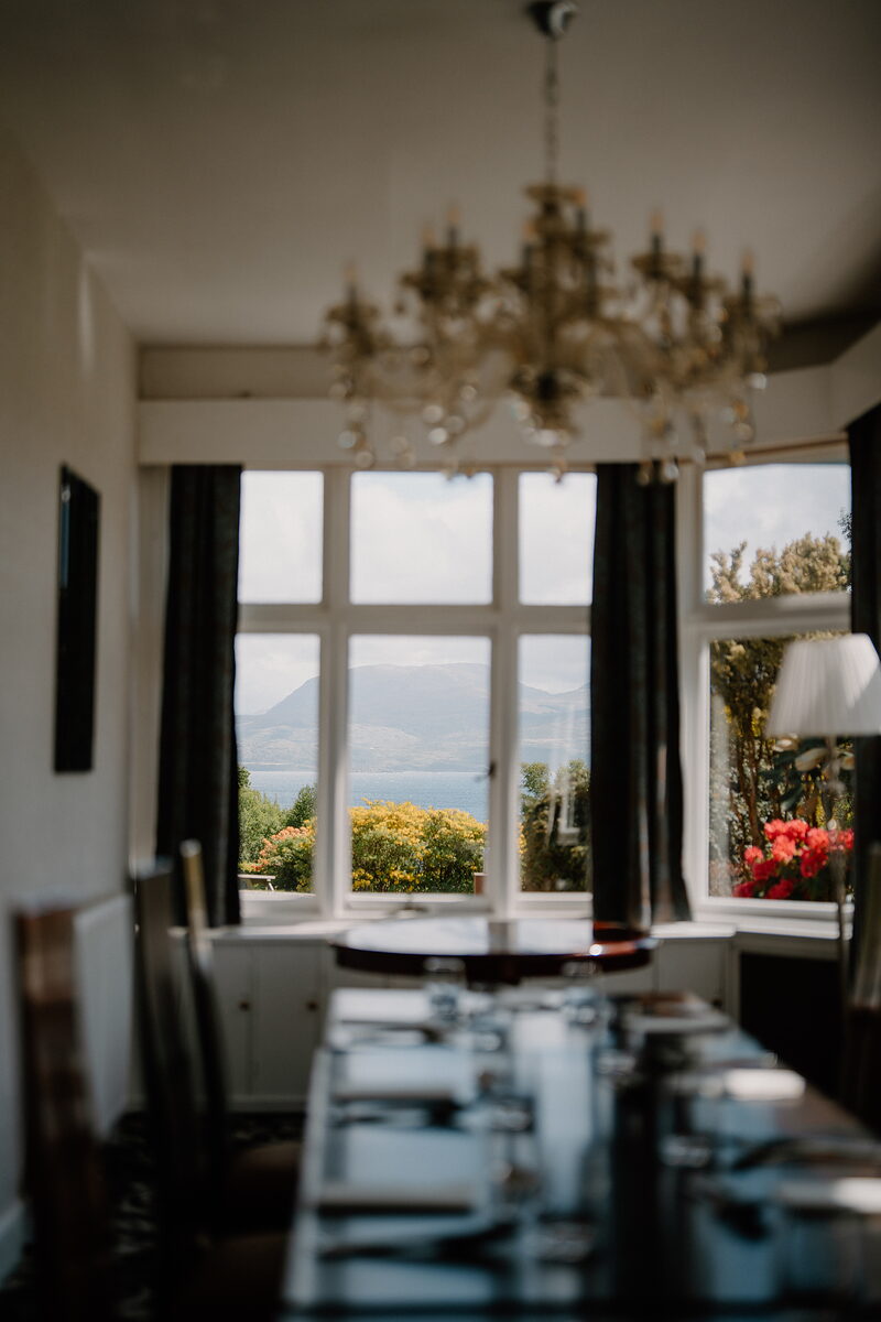 A table set under a brass chandelier in a bay window over the sea loch at Duisdale.