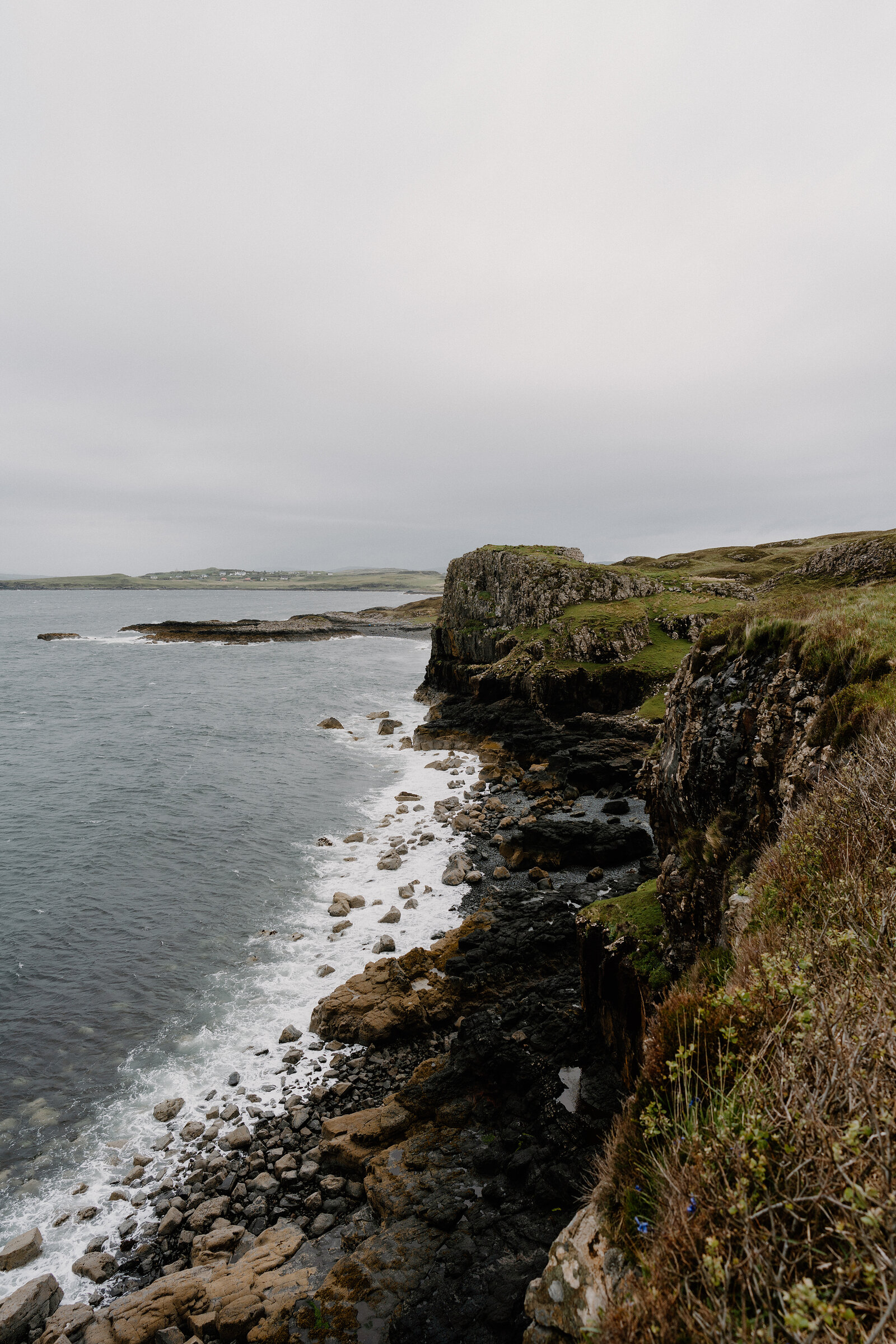 A rugged coastline of dark cliffs and grassy headland meets the sea on the Isle of Skye.