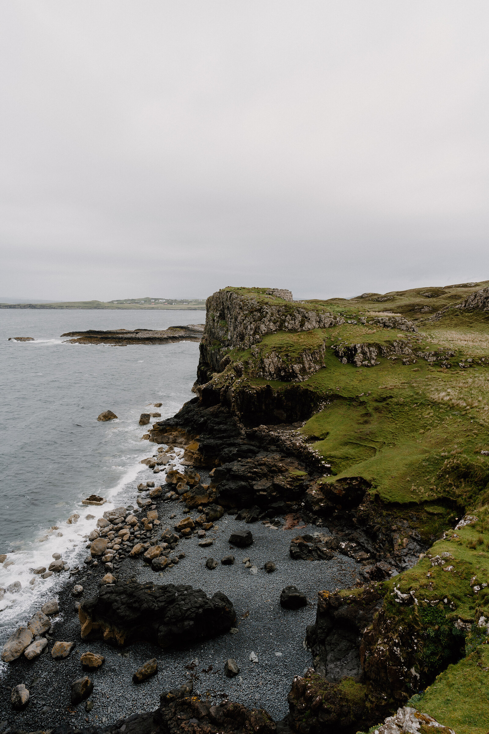 A rugged coastline of cliffs curves toward a distant village on the Isle of Skye.