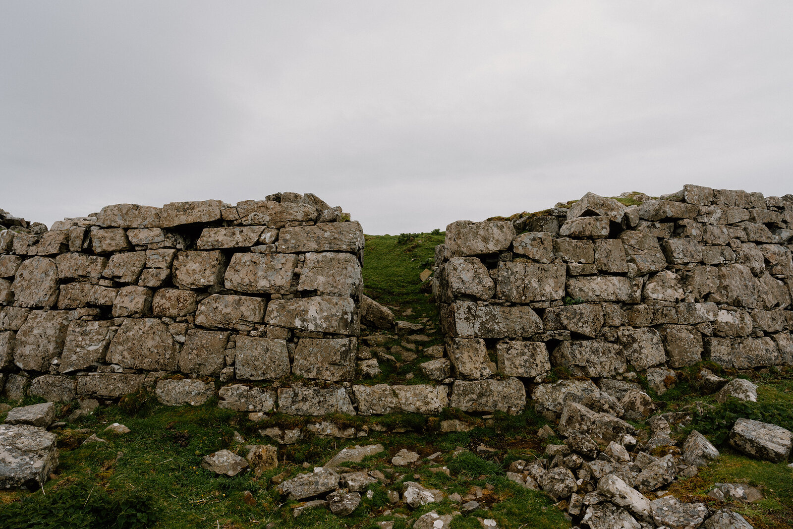 A gap breaks through a dry stone wall on a grassy Skye hillside.