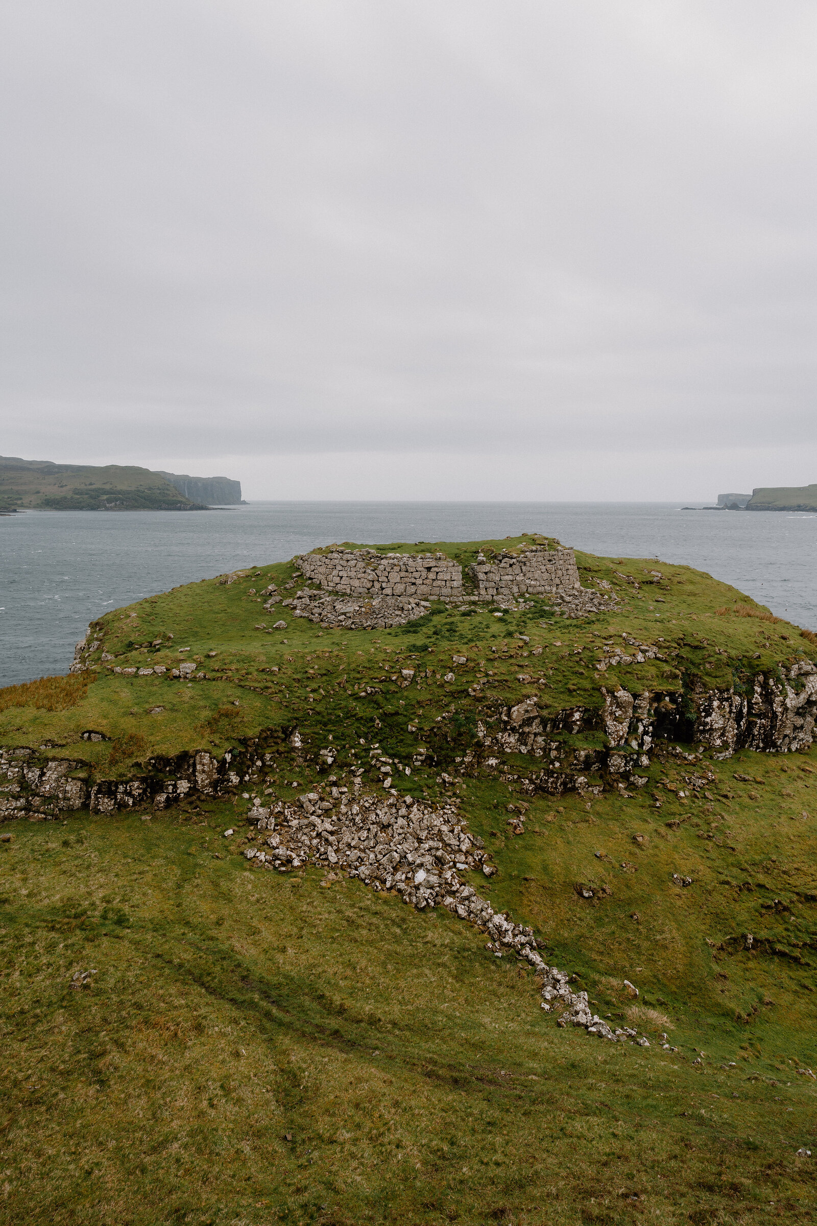 Ruined stone walls crown a grassy headland surrounded by sea on the Isle of Skye.