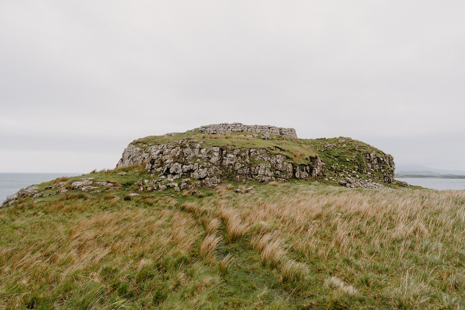 Ruined stone walls crown a grassy headland surrounded by sea on the Isle of Skye.