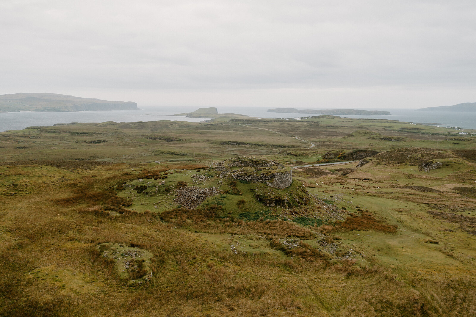 The round ruined fortification sits on its headland, small islands and a village visible in the sea loch beyond on the Isle of Skye.
