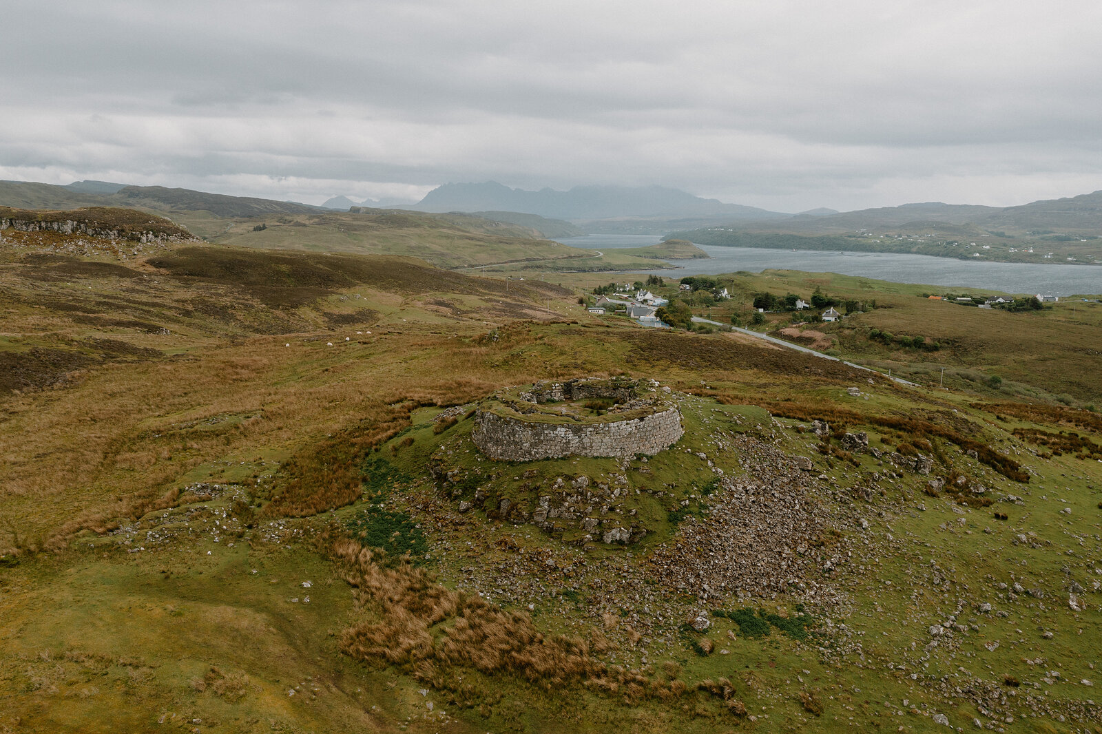 The round ruined fortification sits on its grassy headland above a sea loch and distant hills on the Isle of Skye.