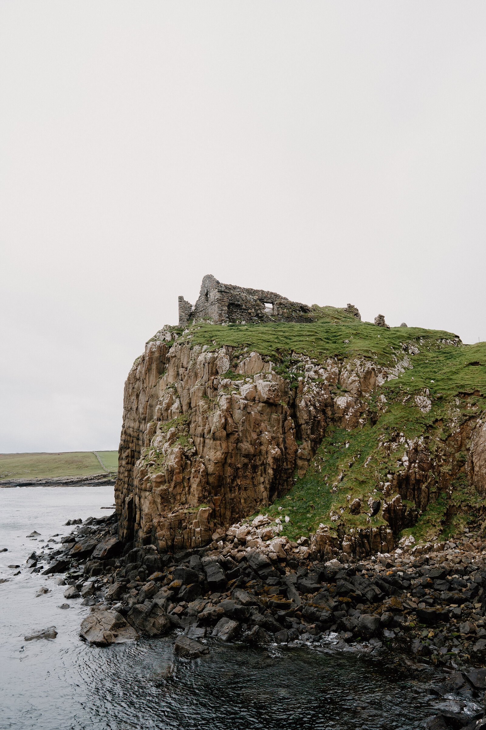 A ruined stone castle stands on a rocky headland above the sea on the Isle of Skye.
