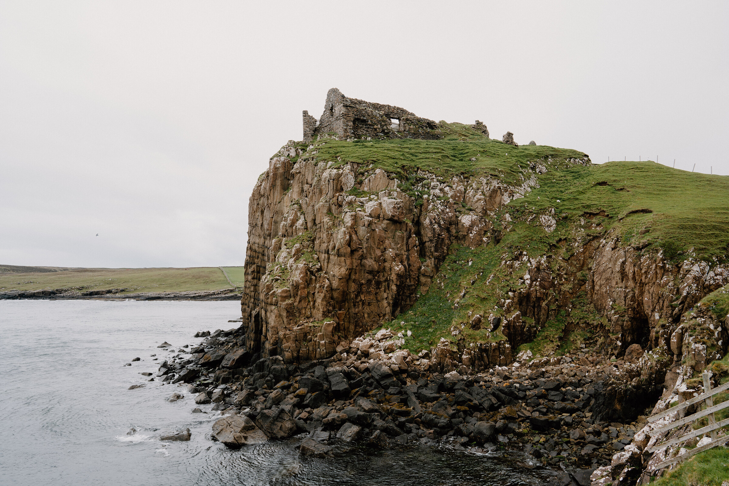 A ruined stone castle stands on a rocky headland above the sea on the Isle of Skye.