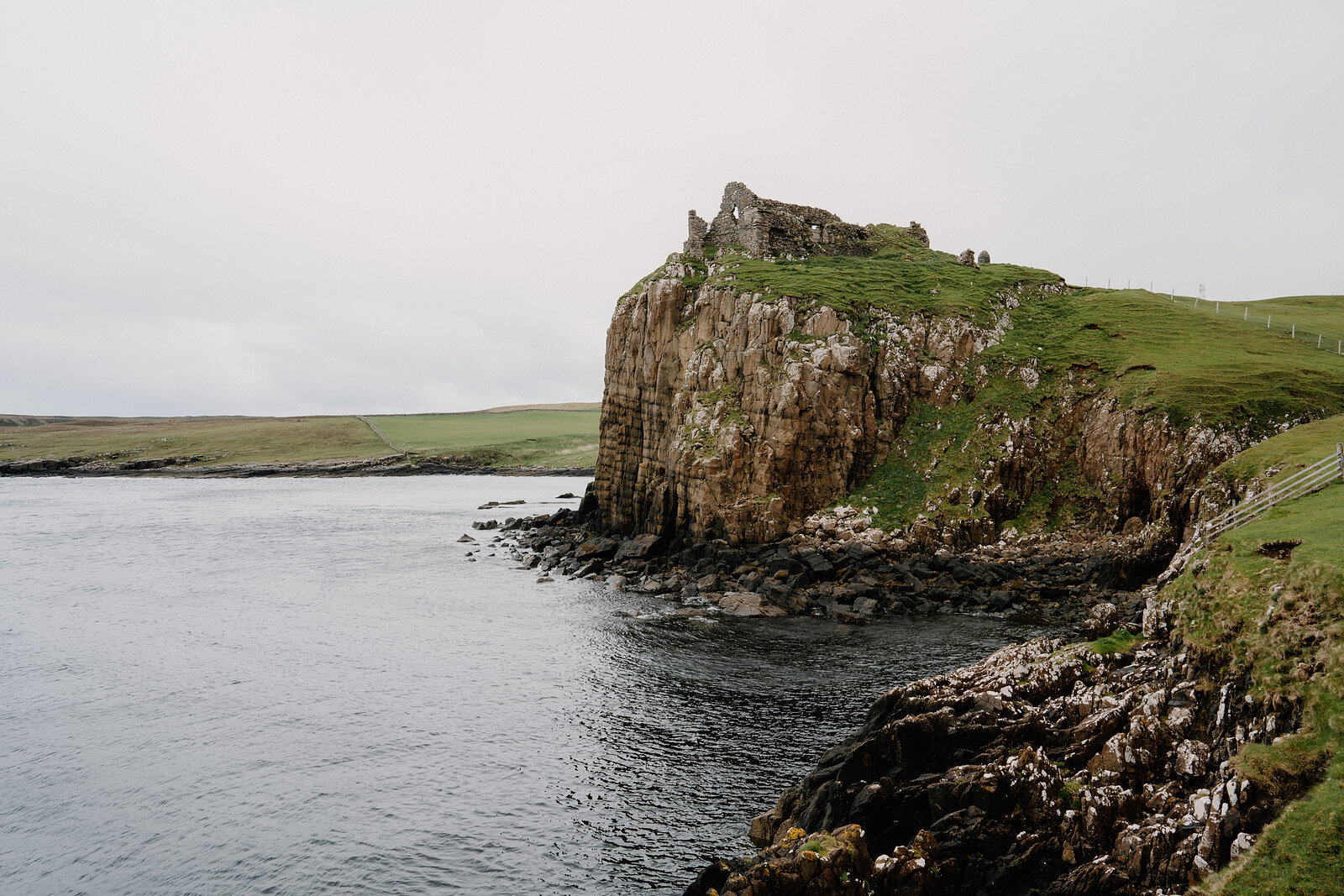 A ruined stone castle stands on a rocky headland, seabirds gathered on the rocks below on the Isle of Skye.