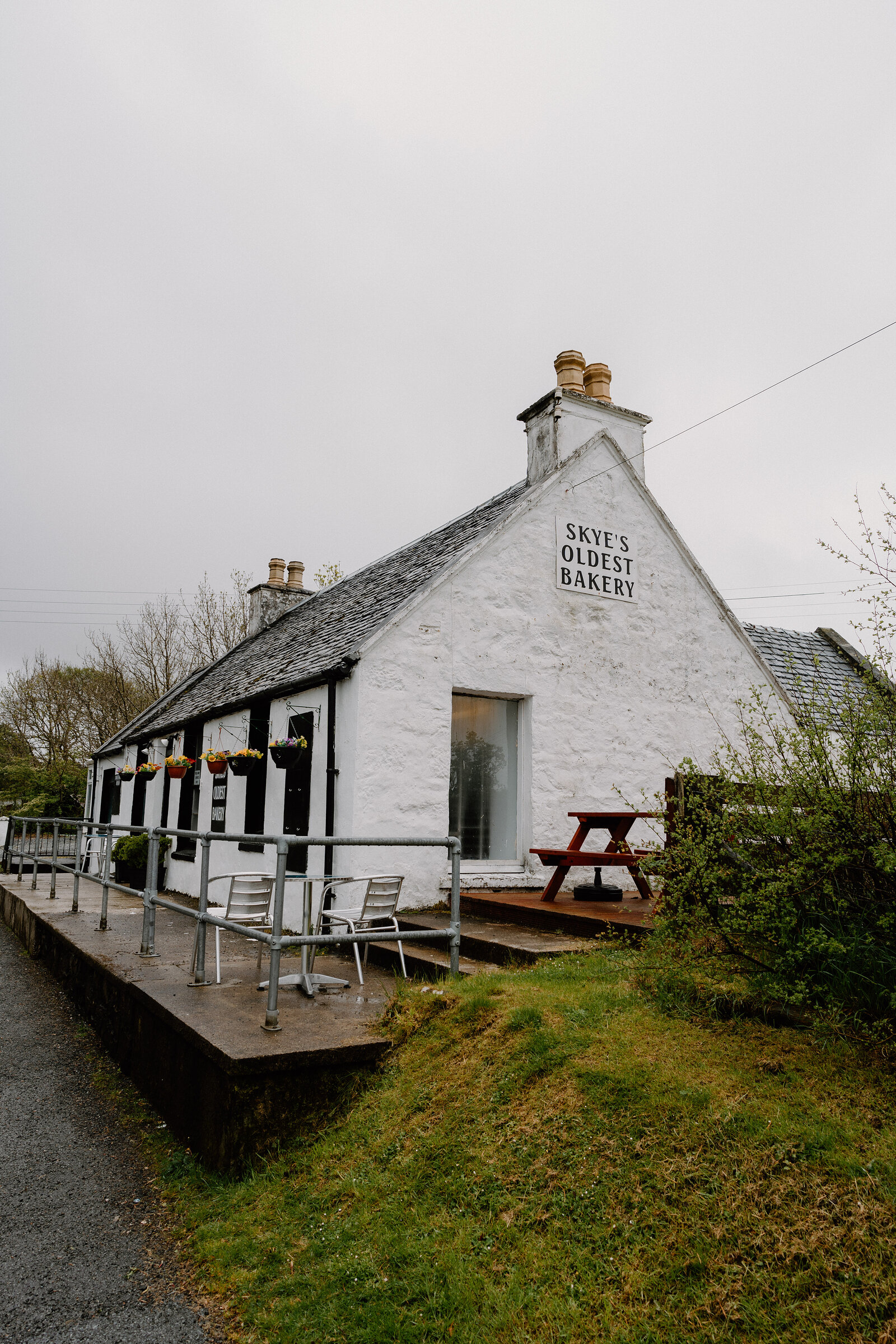 Skye's Oldest Bakery's whitewashed gable end carries its sign above a picnic bench and metal railings.