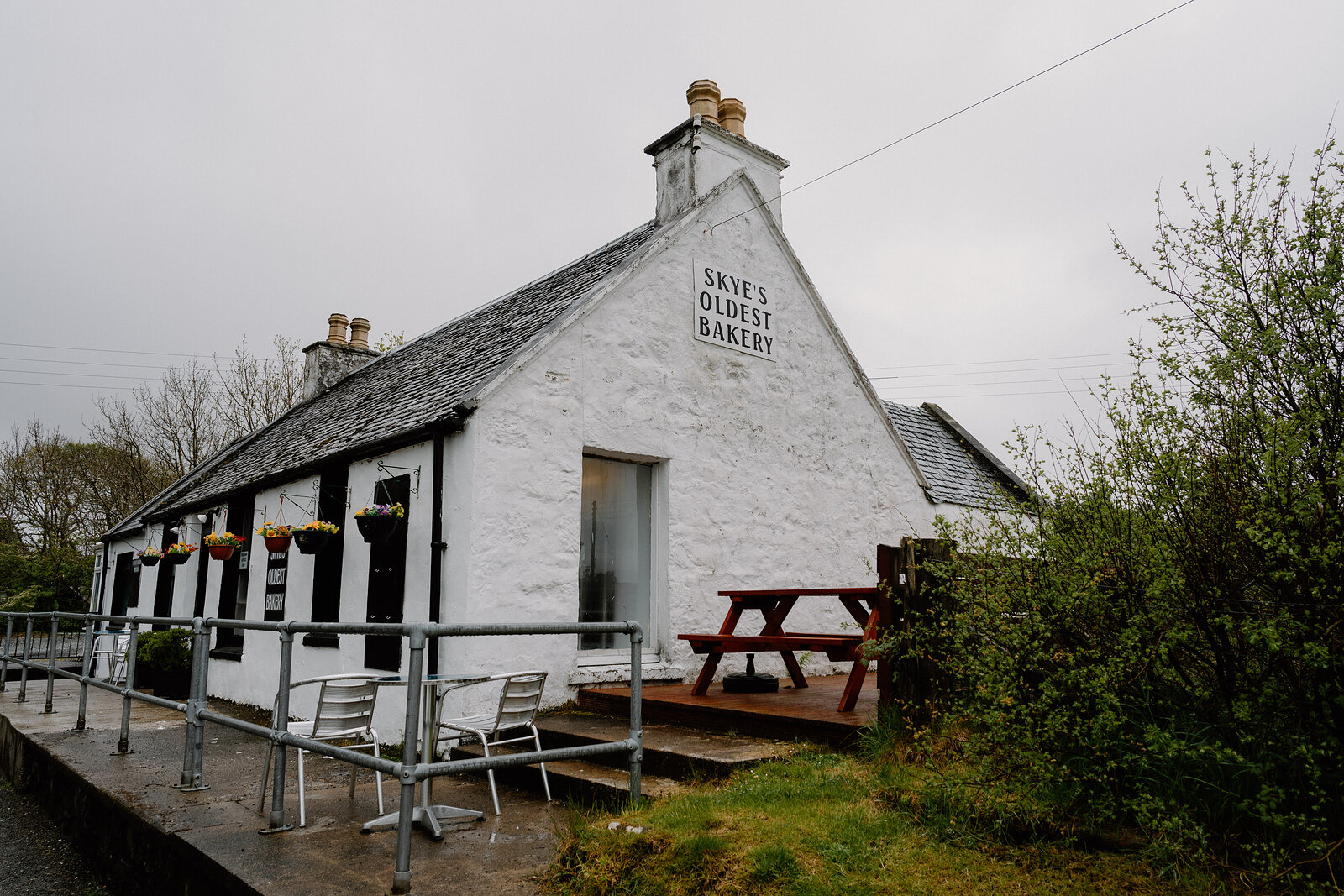 Skye's Oldest Bakery's cottage exterior with picnic table and railings sits beside a grassy verge.