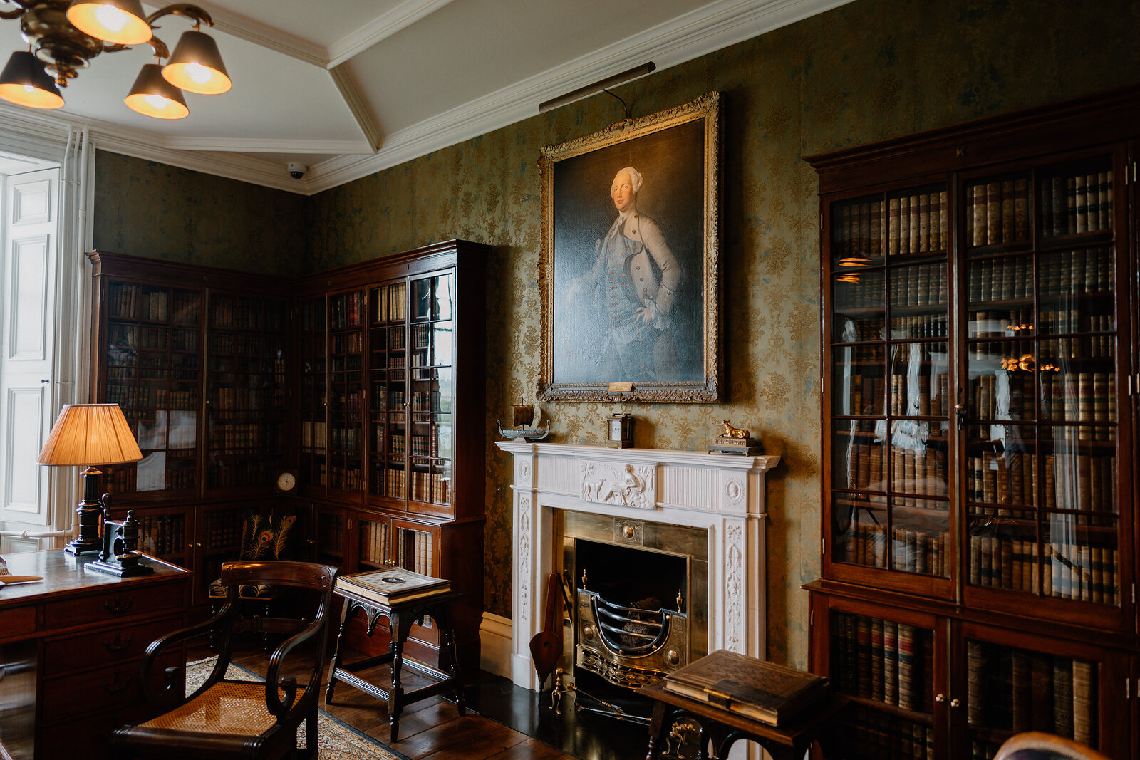A wood-panelled library at Dunvegan Castle has floor-to-ceiling bookshelves either side of a fireplace beneath a large portrait.