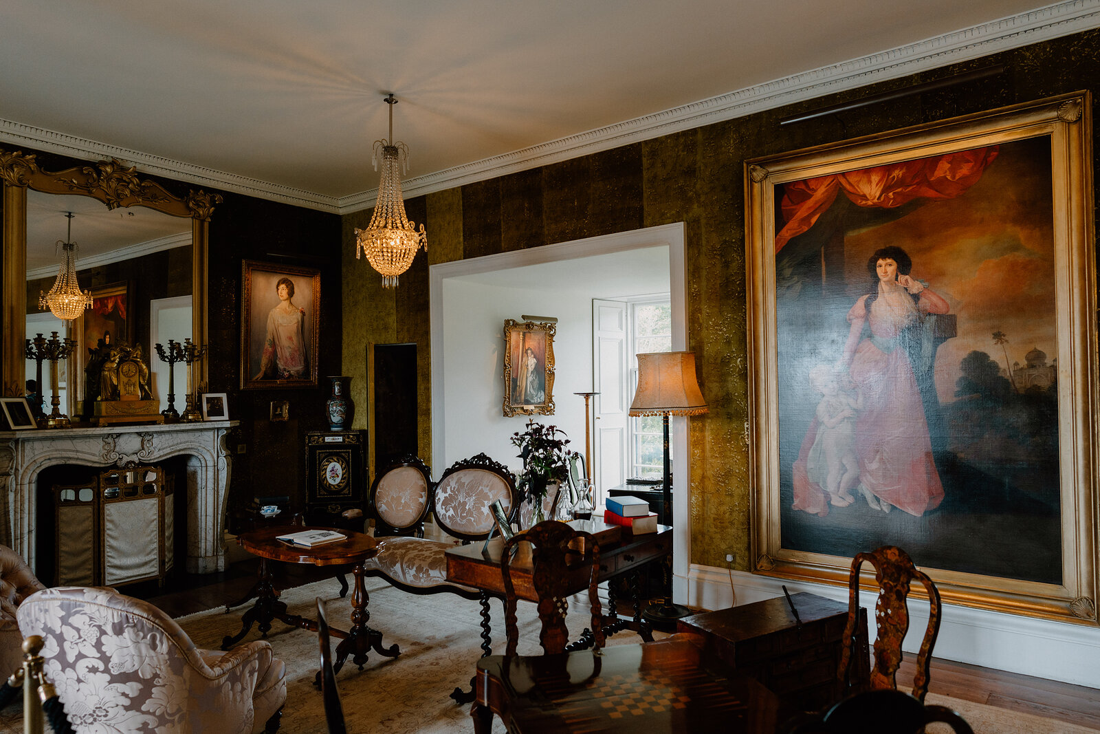 A drawing room at Dunvegan Castle holds antique furniture and gilt-framed portraits beneath a crystal chandelier.