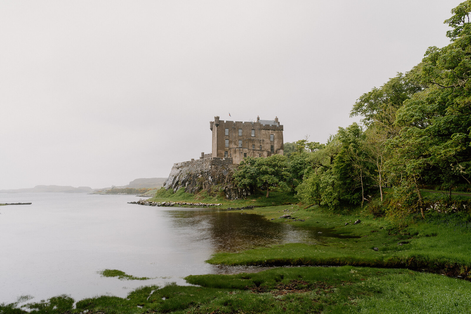 Dunvegan Castle sits on the misty shore of a sea loch, its outline softened by fog.