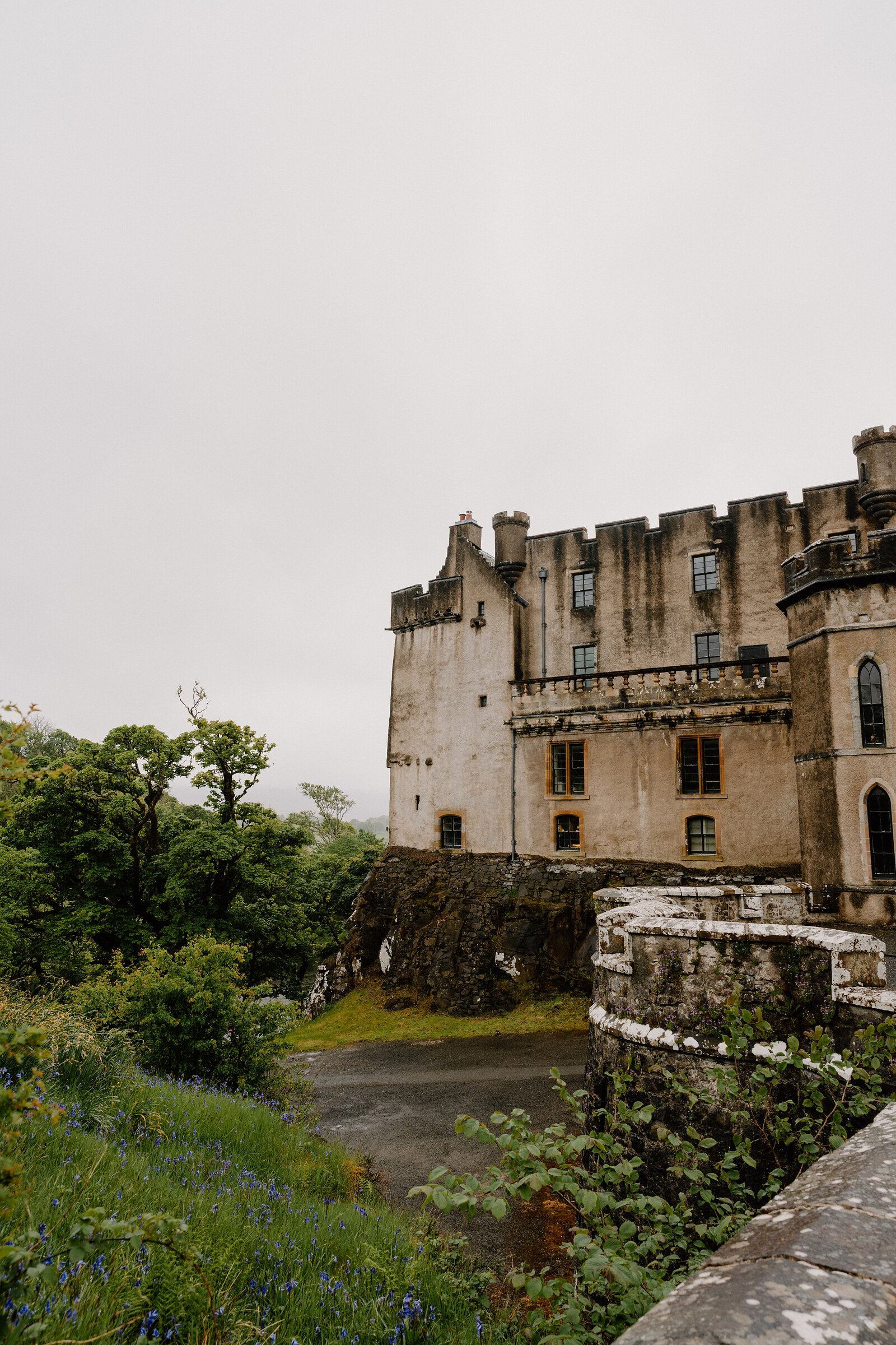 Bluebells grow at the foot of Dunvegan Castle's weathered stone walls and arched windows.