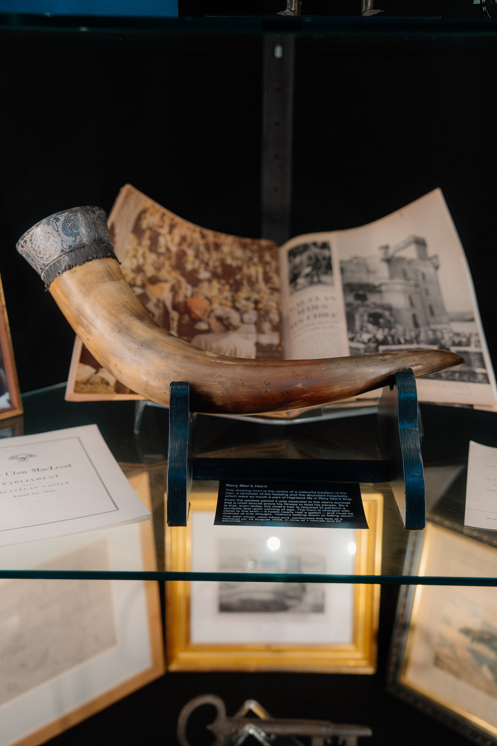 A silver-mounted drinking horn is displayed on a stand beside an open photograph album at Dunvegan Castle.
