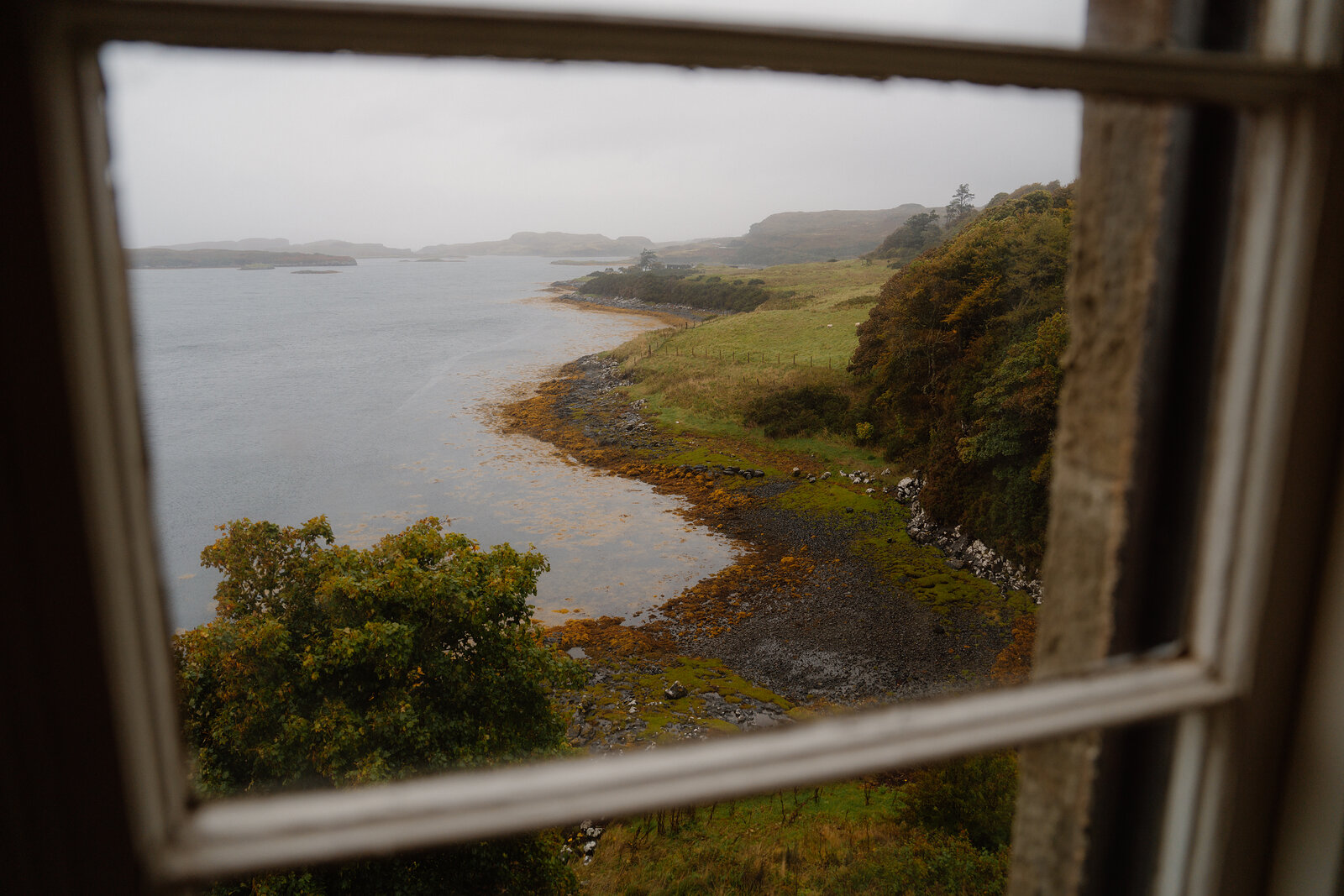 A castle window looks out over a curving loch shoreline dotted with small islands.