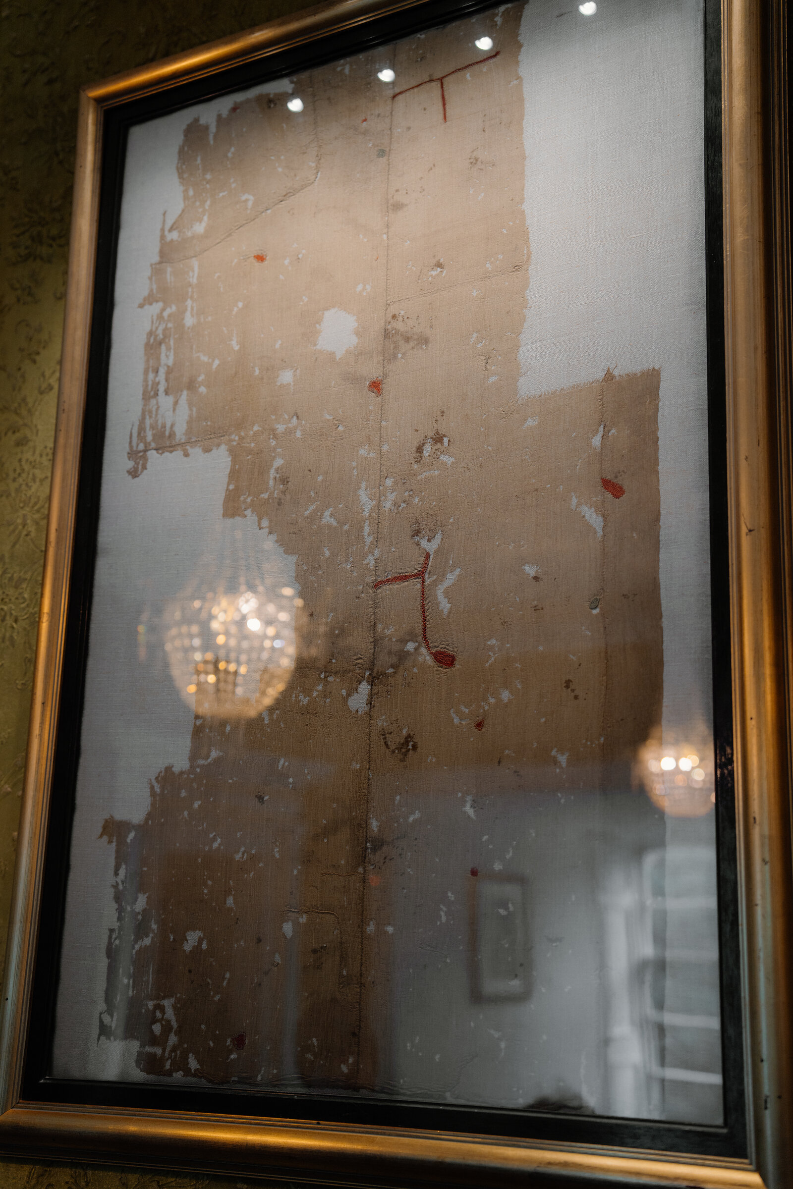 A close view of the Fairy Flag of Dunvegan shows its torn, faded silk behind reflective glass.