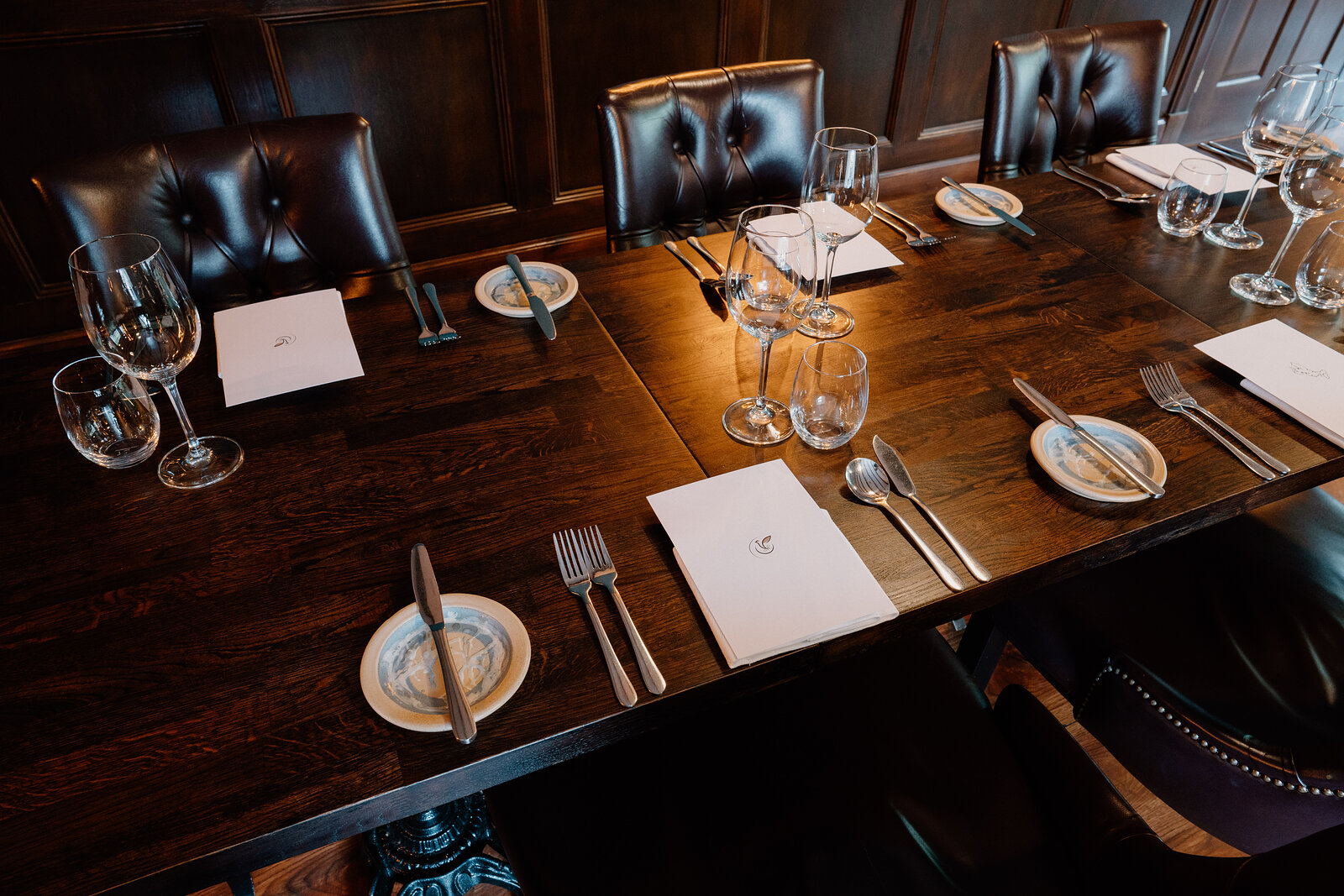 Wine glasses and folded napkins are set on a dark wooden table between high-backed leather chairs at Edinbane Lodge.