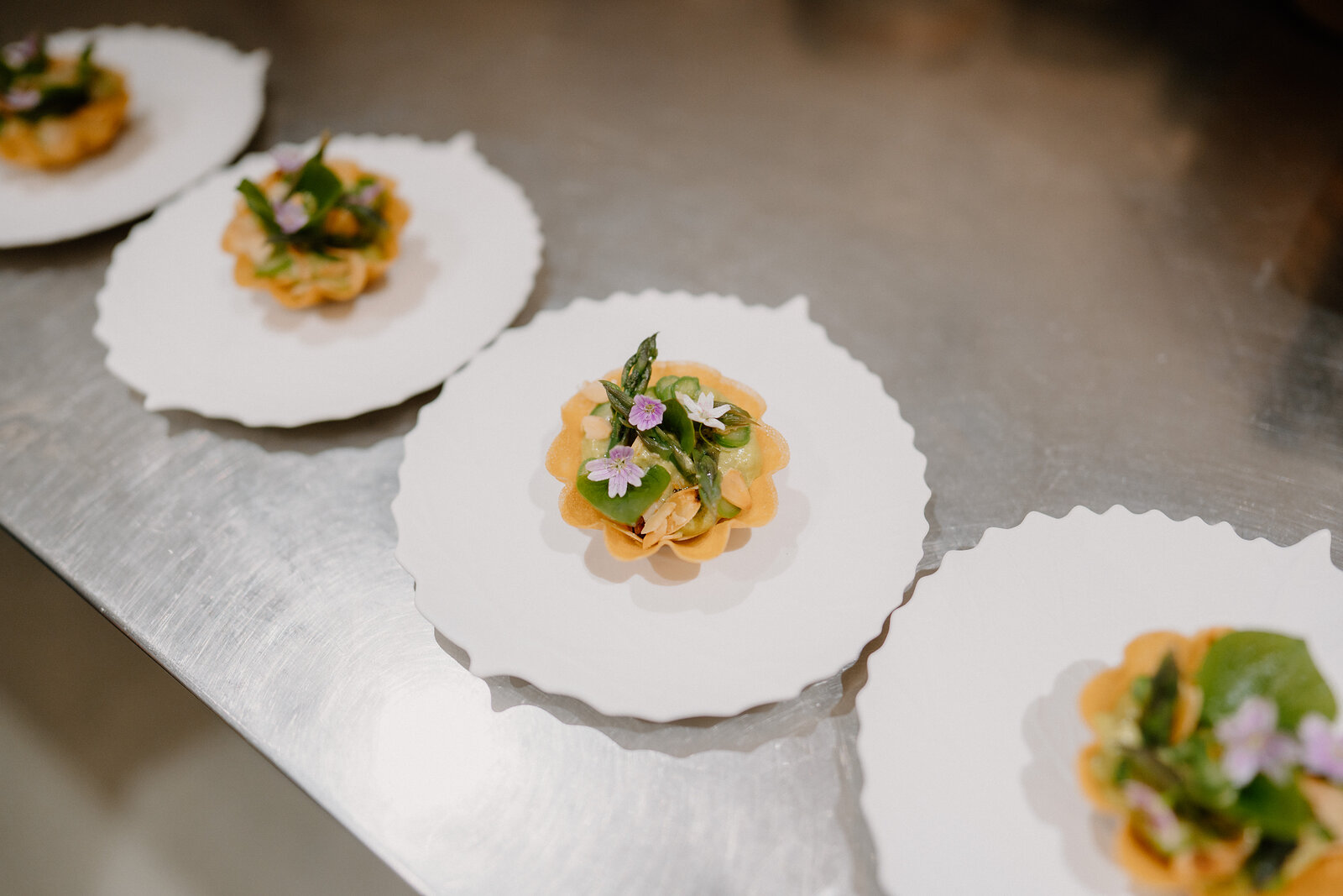 Tartlet canapés topped with edible flowers and herbs are arranged on scalloped white plates at Edinbane Lodge.