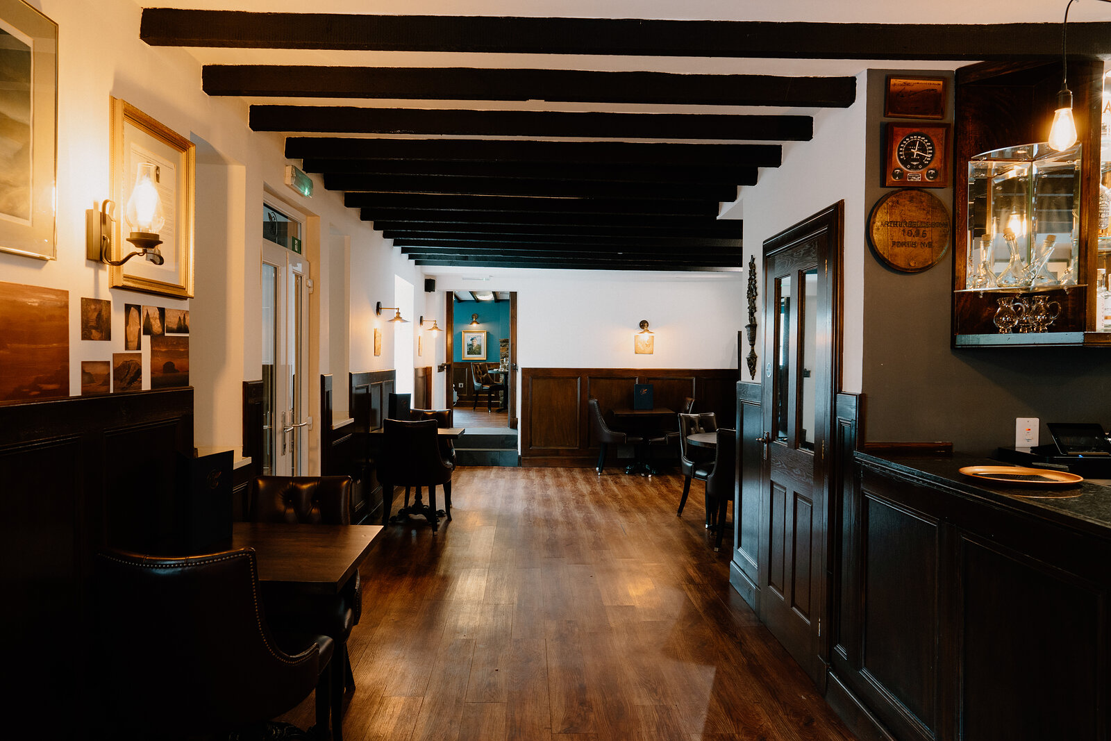A wood-panelled corridor with black beams and wall sconces leads past a bar and seating area at Edinbane Lodge.