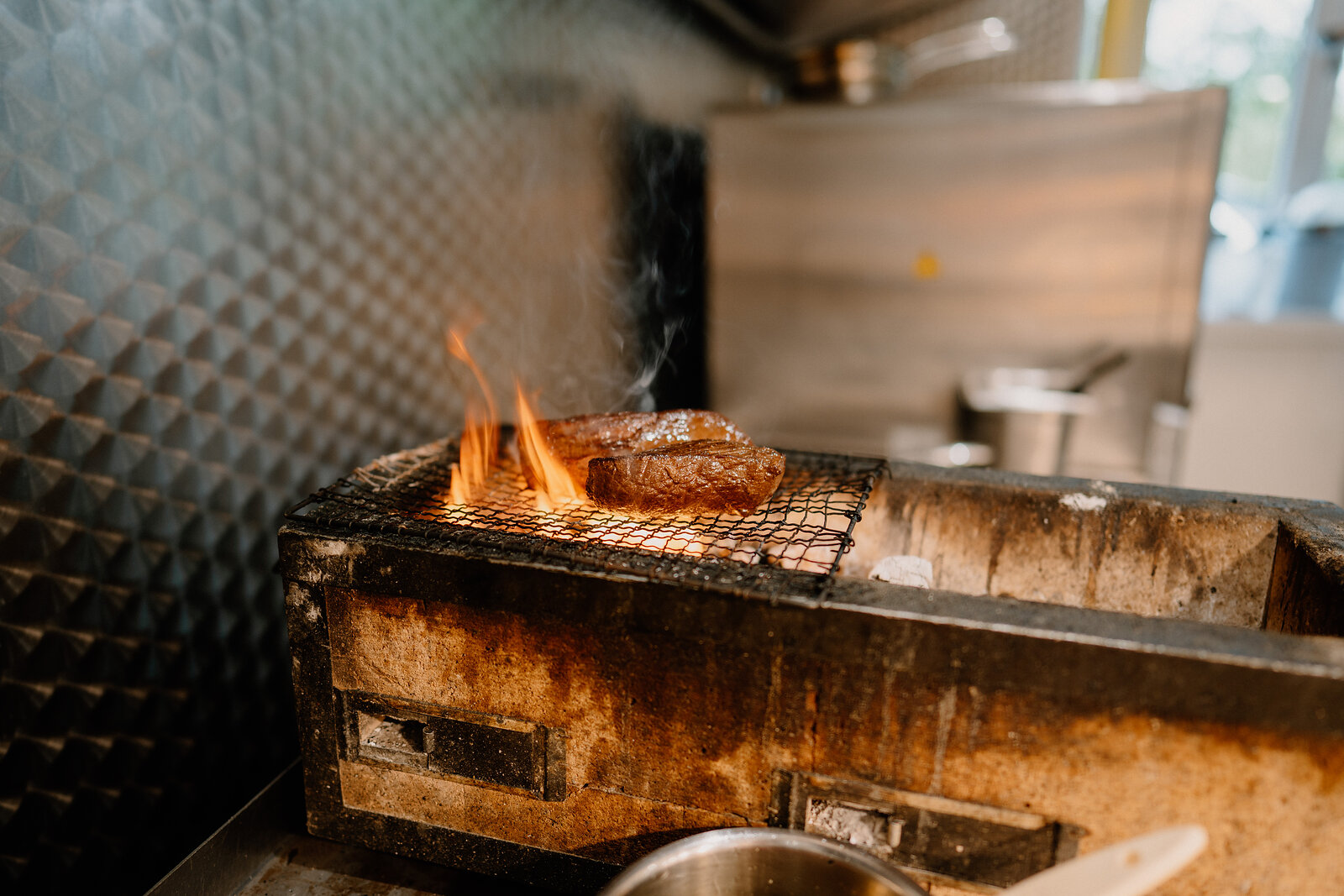 Meat sears over open flames on a mesh rack set into a charcoal grill at Edinbane Lodge.