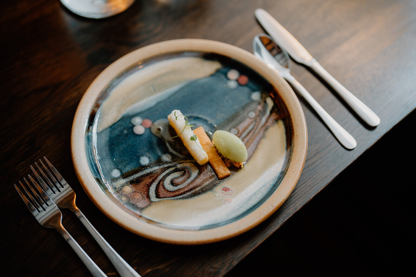 A small fish course sits on a hand-glazed stoneware plate beside cutlery at Edinbane Lodge.