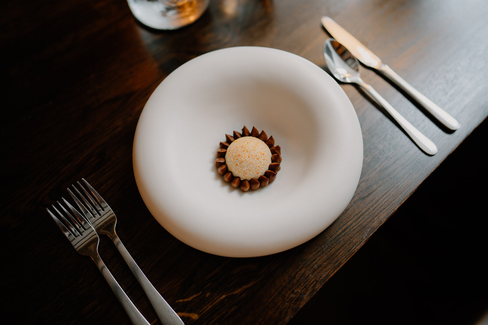 A single dessert truffle on a chocolate base sits on a wide white plate at Edinbane Lodge.