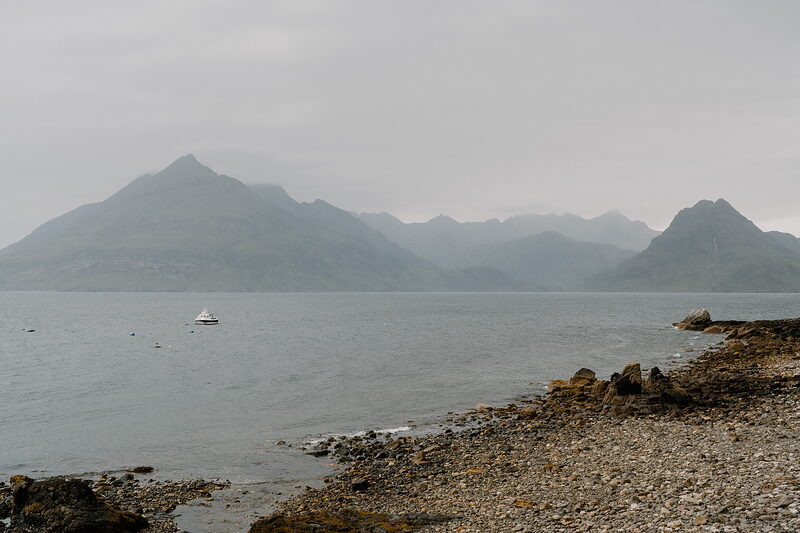 A small boat sits on calm water beneath misty mountains on the Isle of Skye.